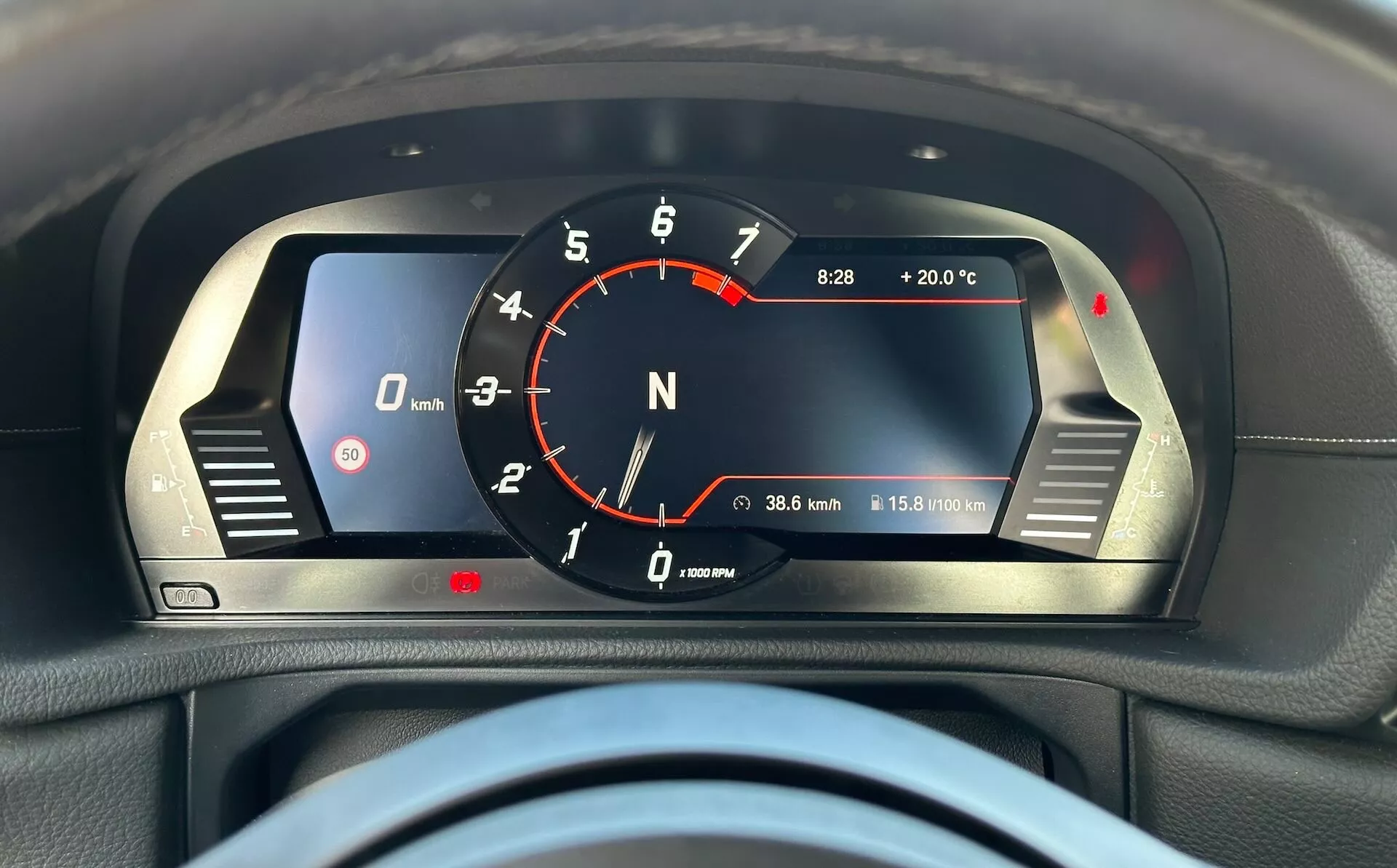Zbliżenie na cyfrowy kokpit Toyoty GR Supra 2019 z czerwonym, analogowym stylem obrotomierza, cyfrowym prędkościomierzem, wskaźnikiem biegu jałowego, cyfrowym zegarem z temperaturą zewnętrzną, licznikiem kilometrów, licznikiem dystansu oraz lampkami ostrzegawczymi, wszystko umieszczone w eleganckiej czarnej obudowie z akcentami w srebrnym kolorze.