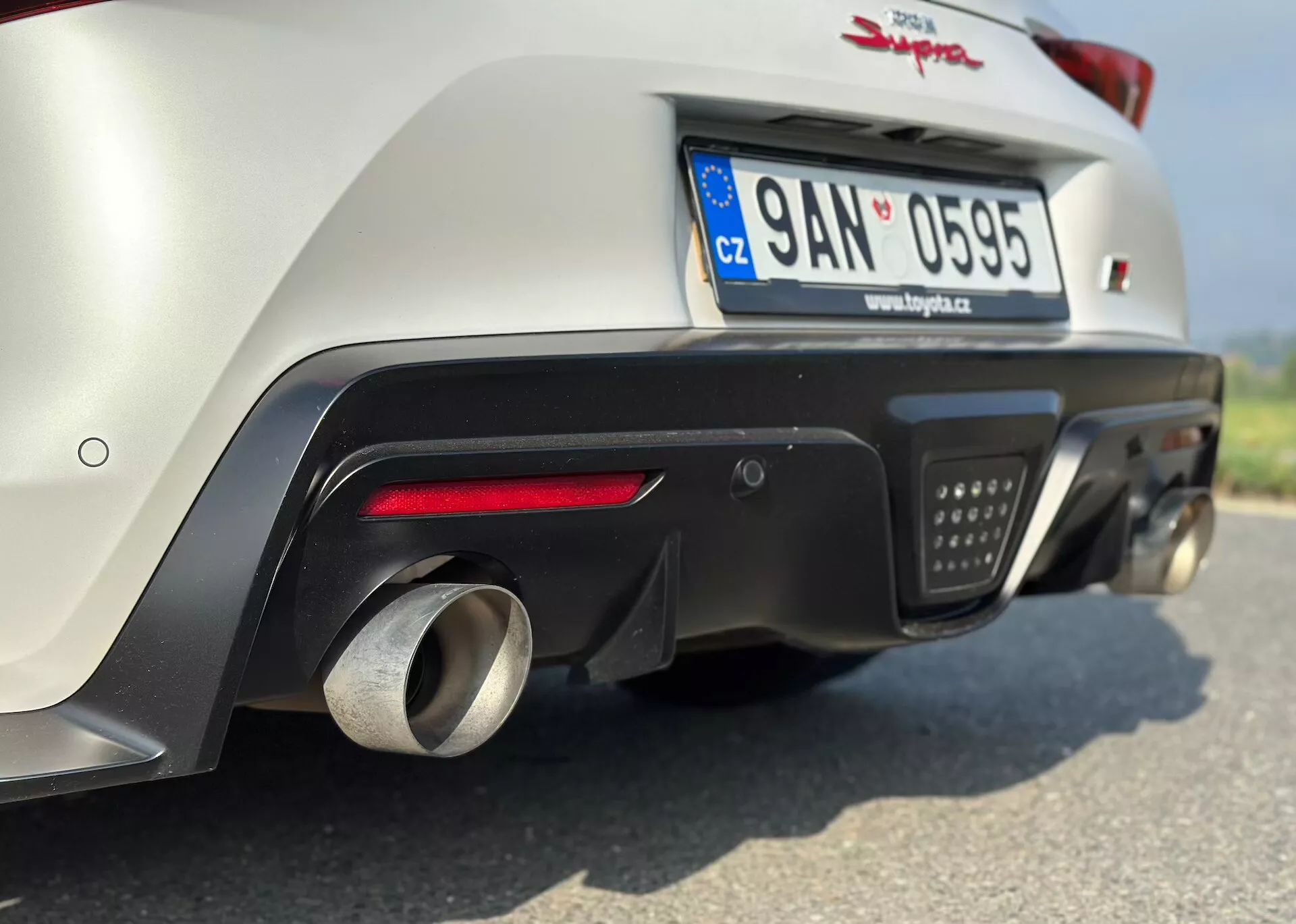Zbliżenie tyłu Toyoty Supra GR z 2019 roku ukazujące dolną część zderzaka, system wydechowy i zaawansowaną aerodynamikę, wykonane z niskiego kąta, aby podkreślić cechy związane z wydajnością, zaparkowany z tablicą rejestracyjną Czech.