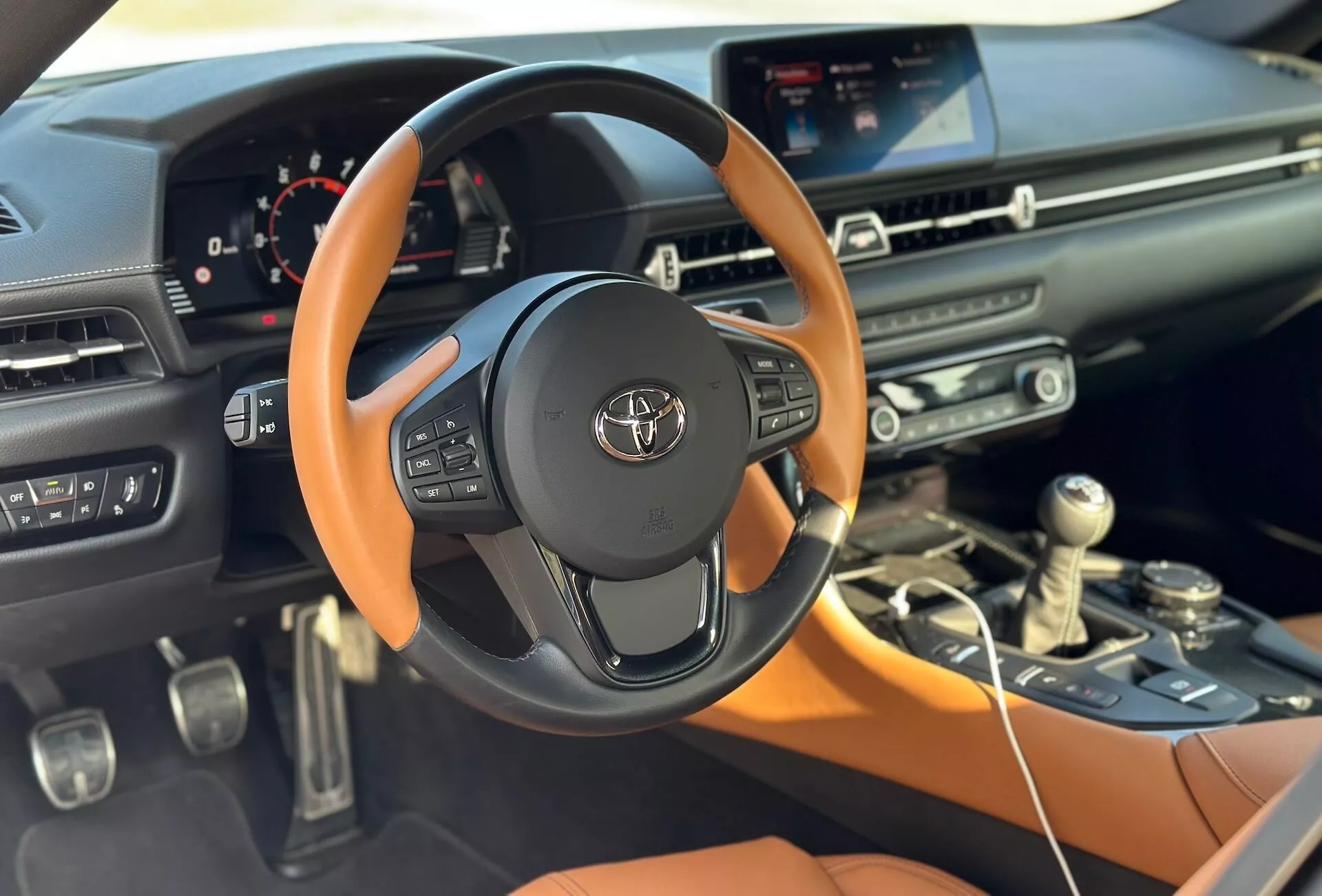Szczegółowy widok wnętrza Toyota Supra 2019 GR-Supra prezentujący kierownicę z emblematem Toyoty, konsolę środkową, ekran systemu infotainment dotykowy oraz częściową deskę rozdzielczą pasażera ze skupieniem na elementach technologicznych i projektowych