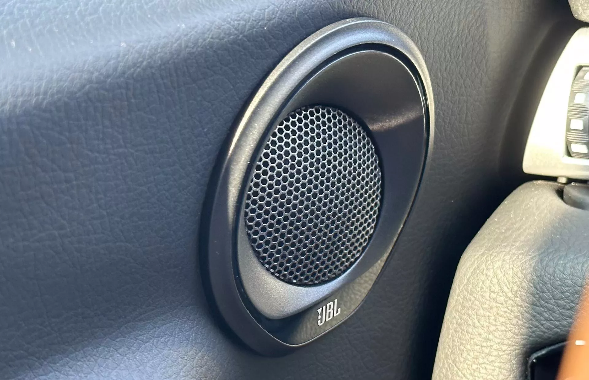 Zbliżenie na głośnik marki JBL zamontowany na ciemnym panelu drzwiowym Toyoty Supra 2019, z heksagonalną kratką z wzorem plastru miodu dla lepszej jakości dźwięku.