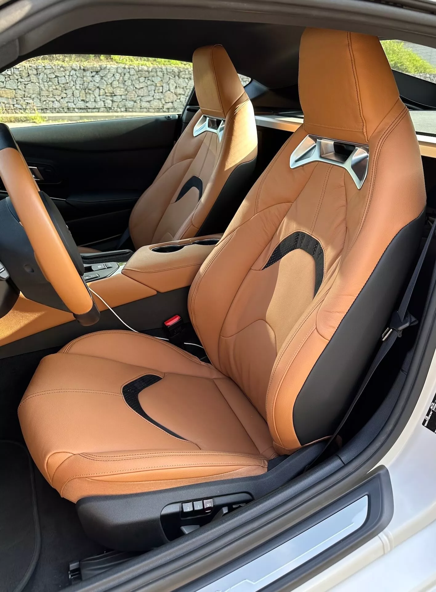 Wnętrze Toyoty GR Supra 2019 pokazujące luksusowe przednie siedzenia z dwukolorowej skóry z elektryczną regulacją, sportowe elementy designu i centralną konsolę z dźwignią zmiany biegów