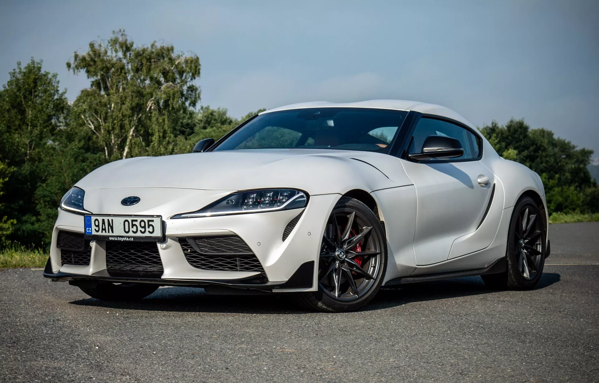 Toyota Supra GR 2019 w świetle dziennym ukazująca aerodynamiczny design, agresywny przód z dużymi wlotami powietrza i eleganckimi reflektorami, profil boczny z felgami aluminiowymi i hamulcami wysokiej wydajności, oraz wysokiej jakości wykończenie lakieru.