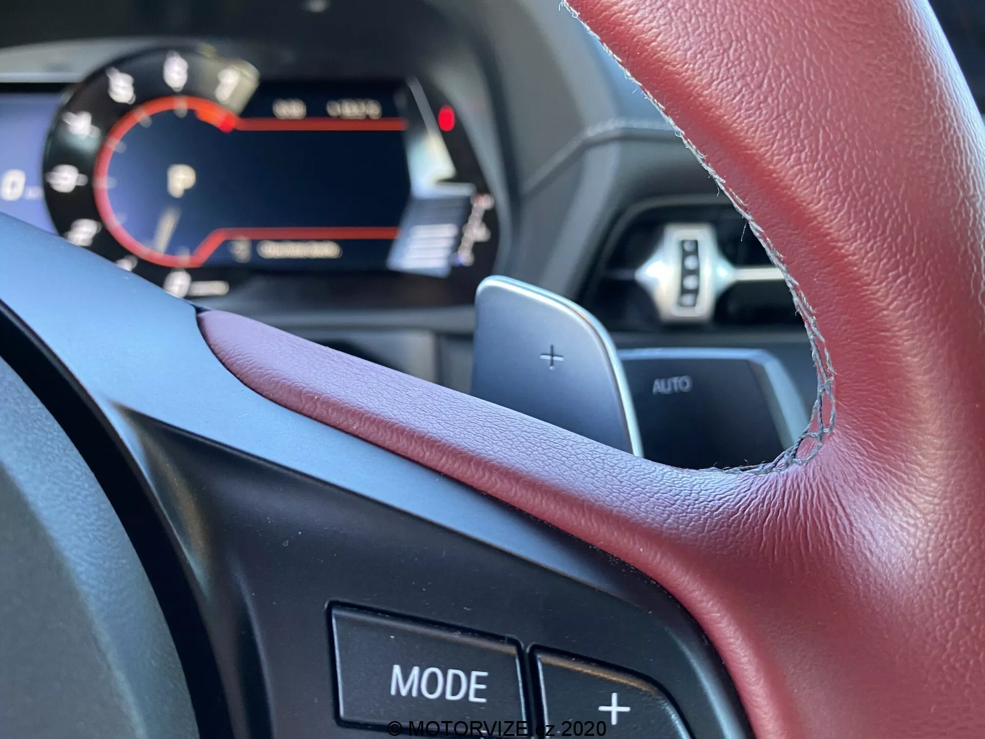 Widok wnętrza Toyoty Supry 2019 z perspektywy kierowcy, koncentrujący się na wielofunkcyjnej kierownicy z łopatkami do zmiany biegów i różnymi przyciskami sterującymi. Część cyfrowej deski rozdzielczej z nowoczesnymi elementami wyświetlacza jest widoczna nad górnym brzegiem kierownicy, podkreślając zaawansowane funkcje technologiczne samochodu.