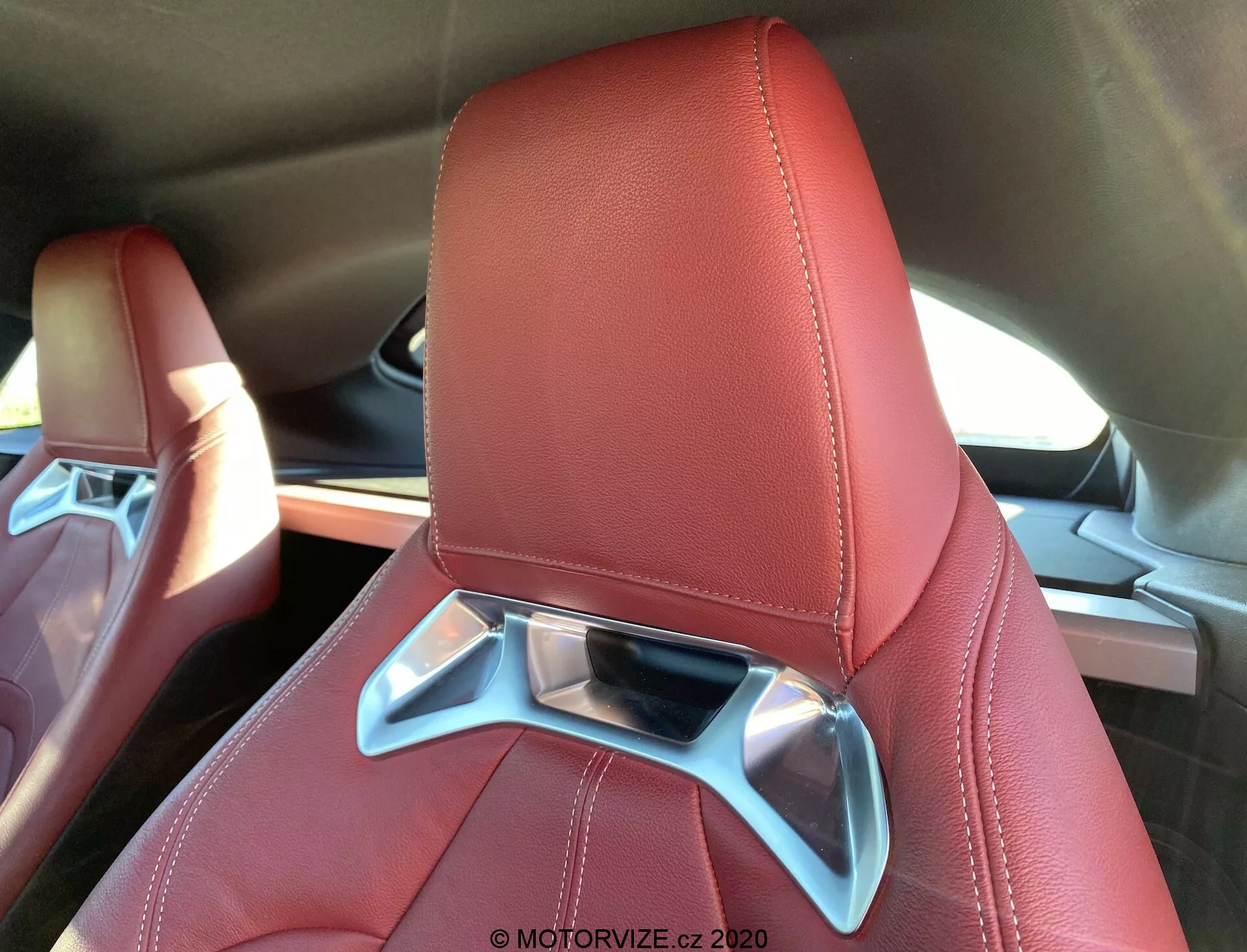 Toyota Supra 2019 GR Supra 2.0 Pure Automatic: Szczegół luksusowego i nowoczesnego fotela samochodowego obitego czerwoną skórą z widocznymi przeszyciami, z zintegrowanym zagłówkiem z chromowanym elementem dekoracyjnym, widziany z górnej tylnej perspektywy.
