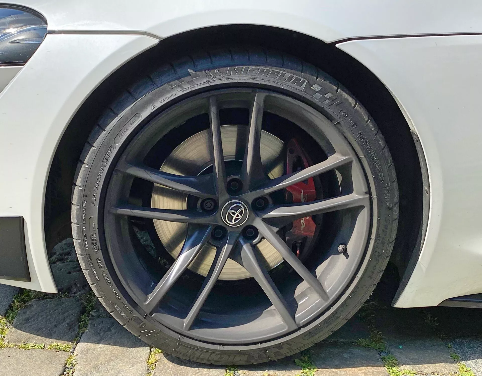 Zbliżenie na przednie koło samochodu, skupiające się na stronie kierowcy z pięcioramienną czarną felgą aluminiową, czerwonym zaciskiem hamulca i oponą marki Pirelli, sugerujące sportowy i wydajnościowy wygląd.