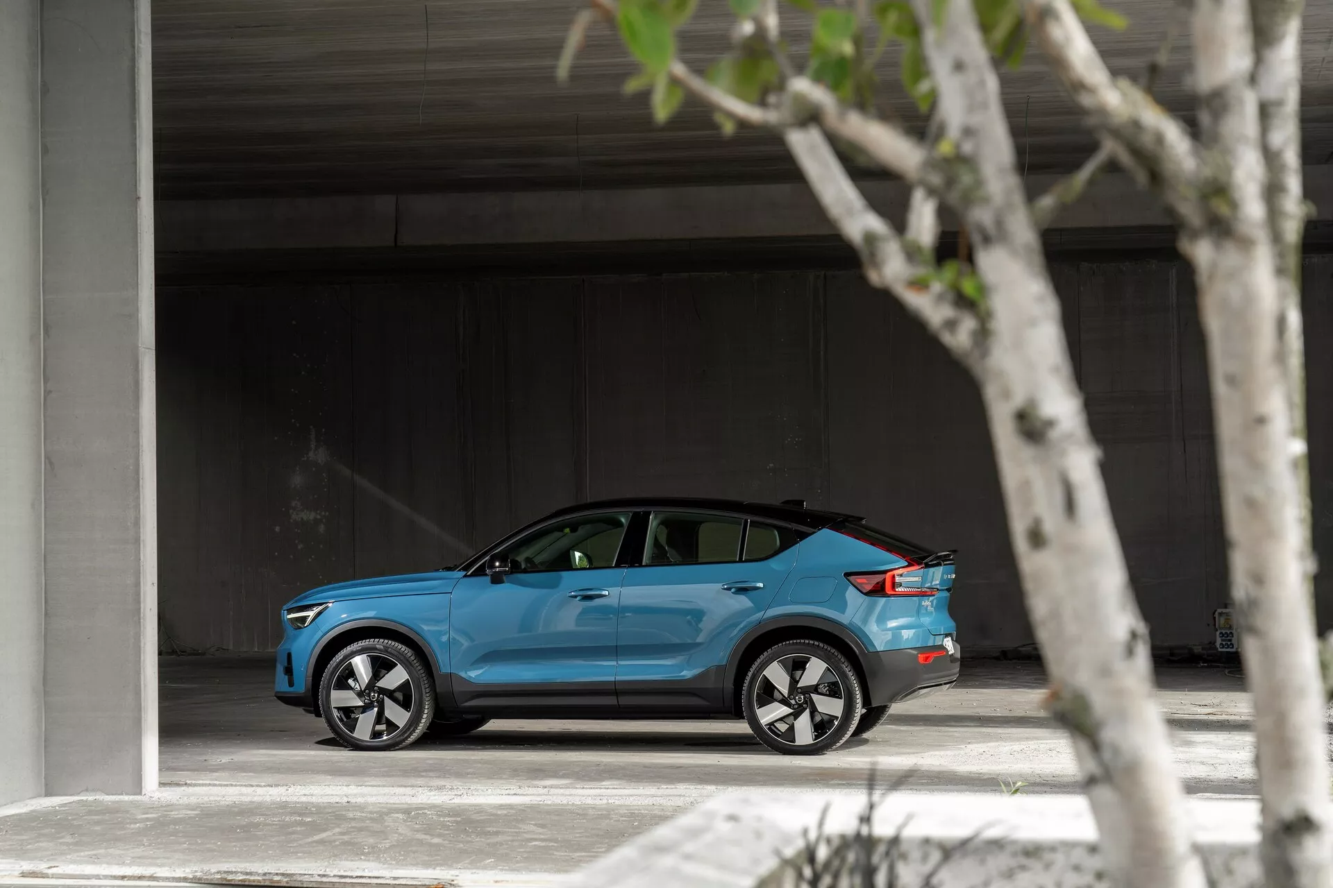 Profil boczny jasnoniebieskiego Volvo C40 z 2021 roku zaparkowanego na przestronnym terenie, prezentującego swój elegancki, nowoczesny design, srebrne wieloramienne felgi aluminiowe, lekko przyciemniane szyby oraz potencjalną pokrywę portu ładowania.