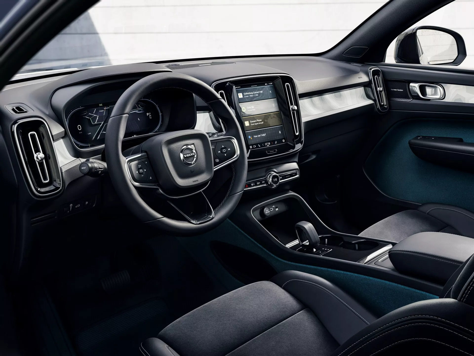 Zdjęcie wnętrza Volvo C40 2021 (1. generacja) z perspektywy zewnętrznej, ukazujące kokpit kierowcy z kierownicą, cyfrowym zestawem wskaźników, konsolą centralną z dotykowym systemem infotainment, sterowaniem klimatyzacją, ergonomicznymi siedzeniami z ciemnego materiału, przyciskami sterowania drzwi i dwukolorowym schematem z nowoczesnymi, funkcjonalnymi elementami designu.