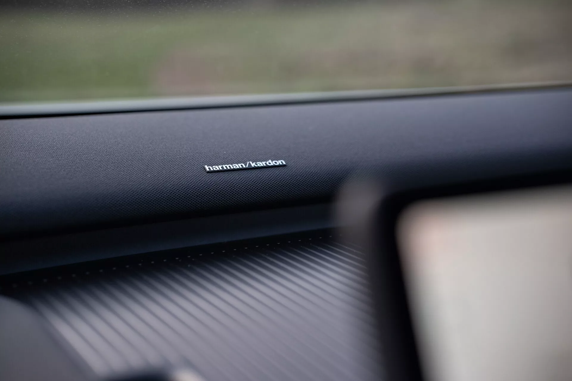 Zdjęcie wnętrza Volvo EX30 2024 skupione na brandingu systemu audio Harman/Kardon na desce rozdzielczej po stronie pasażera, prezentujące wysokiej jakości materiał i podkreślające zaawansowaną technologię systemu dźwiękowego.