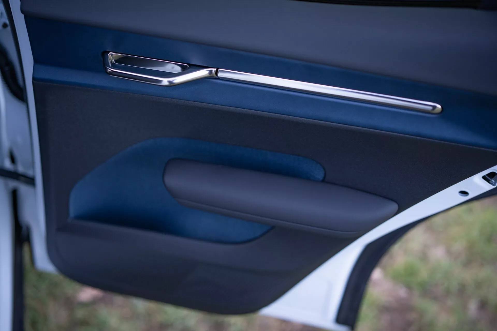 Zbliżenie wnętrza drzwi Volvo EX30 2024, prezentujące elegancką metalową klamkę, ergonomiczny podłokietnik i kieszeń na drobiazgi w ciemnym, wysokiej jakości wykończeniu