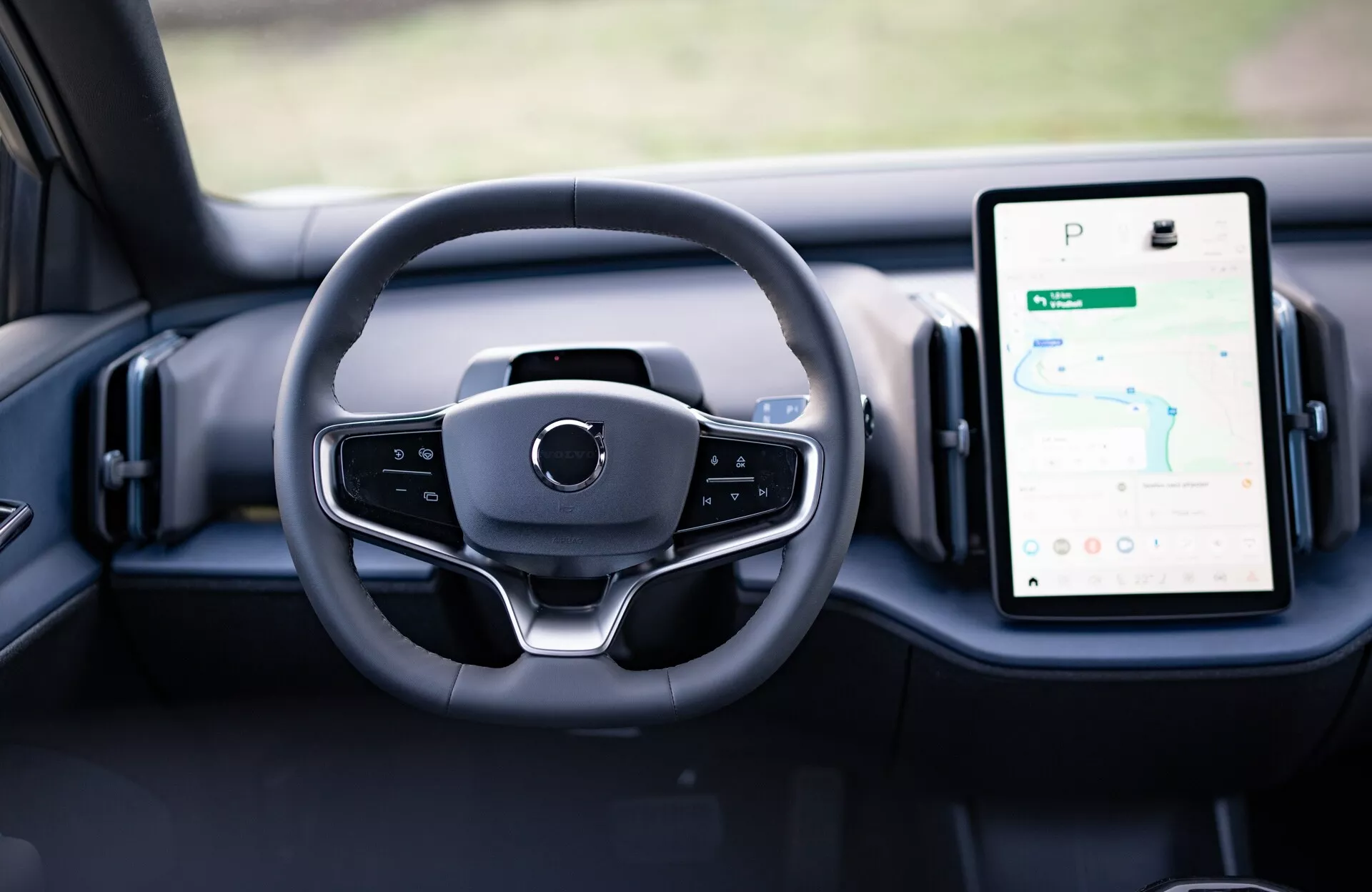 Widok wnętrza Volvo EX30 2024 pokazujący nowoczesny design kierownicy i cyfrowe zegary na desce rozdzielczej, w tym pionowy system infotainment z ekranem dotykowym z GPS.
