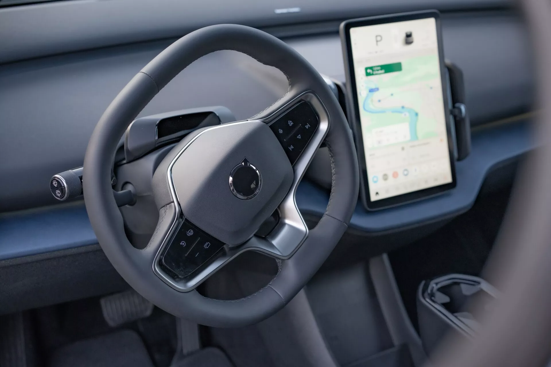 Wnętrze Volvo EX30 2024 z widokiem na strefę kontroli kierowcy z nowoczesną kierownicą płaskim dnem i dużym pionowym ekranem dotykowym do nawigacji i mediów na desce rozdzielczej