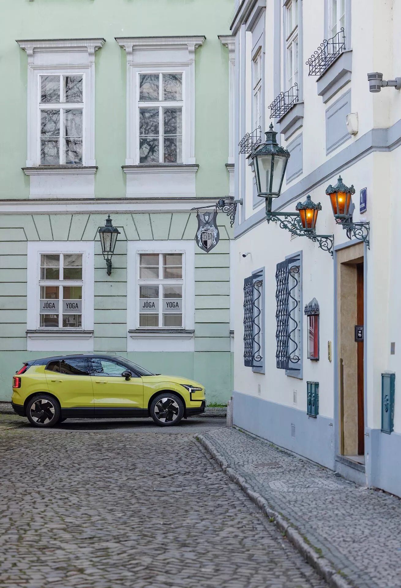 Volvo EX30 2024 zaparkowane na brukowanej ulicy w scenerii starego miasta, uchwycone z trzykwartalnego tylnego kąta, pokazujące prawą stronę i tył samochodu, w tym koła, tylne światła i częściowe detale dachu w jaskrawym żółtym kolorze