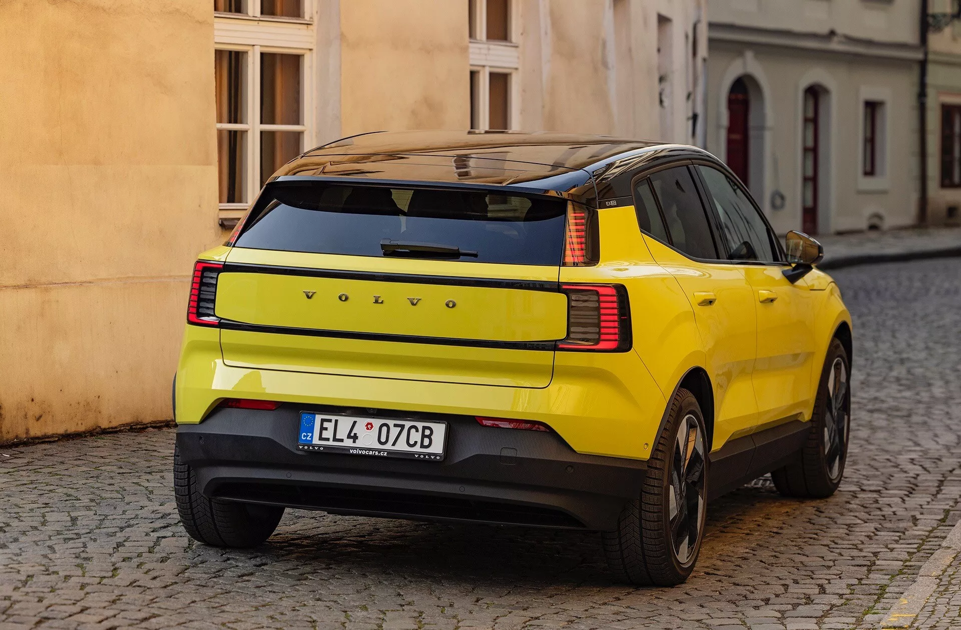 Żółty SUV Volvo EX30 2024 wyświetlający swój charakterystyczny krągły panel tylny, tylne światła LED i funkcje bezpieczeństwa, zaparkowany na brukowanej ulicy z widoku trzech czwartych z tyłu