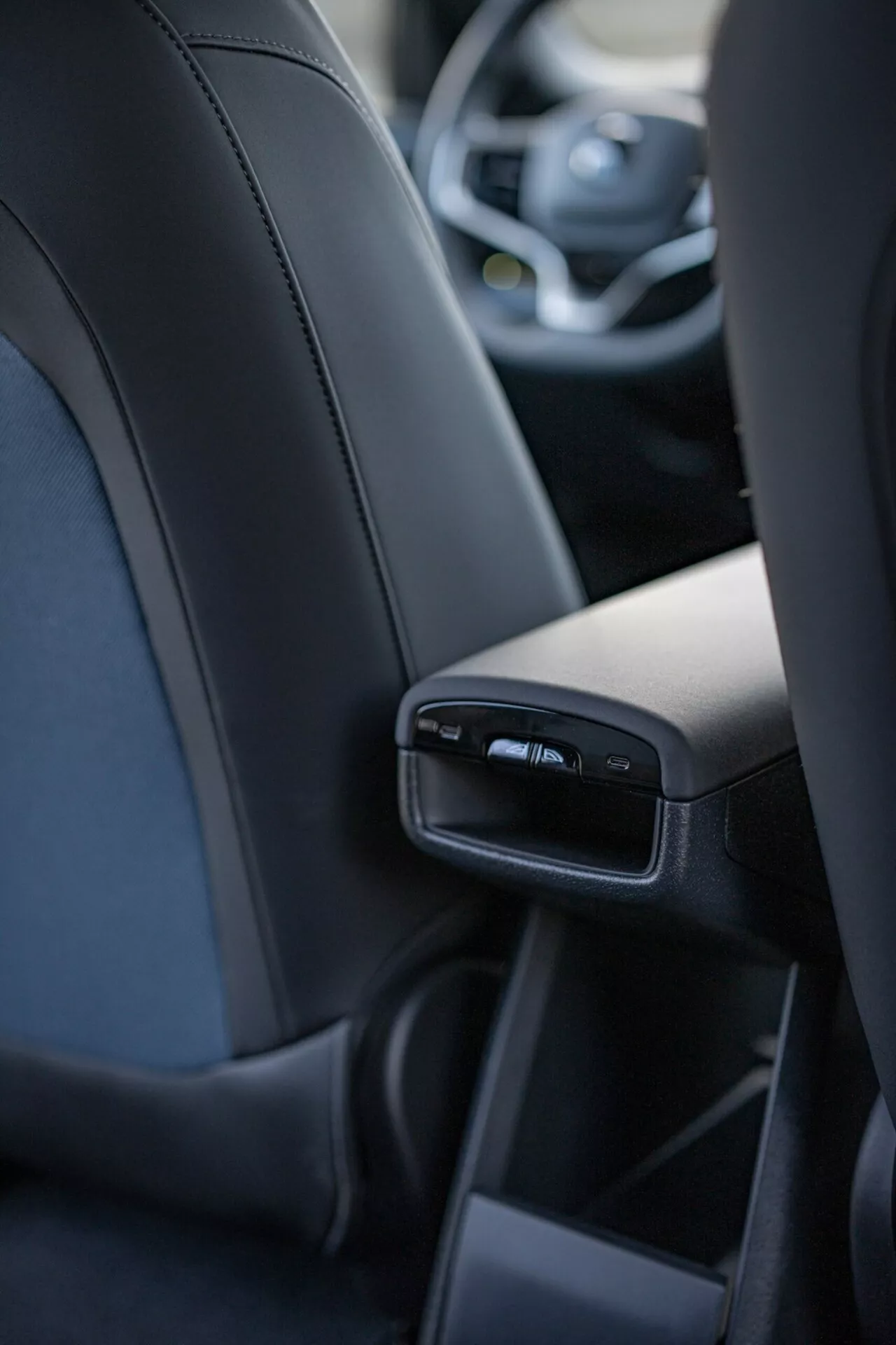 Wnętrze Volvo EX30 2024 skupiające się na szczegółowych funkcjach tylnej konsoli środkowej z perspektywy centralnego tylnego pasażera, w tym porty USB i nawiewy, prezentujące luksus i technologię