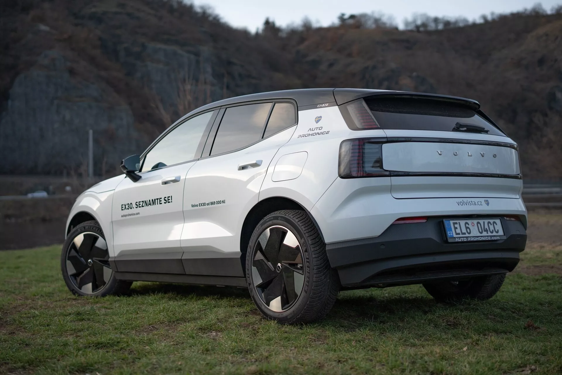 Widok z tyłu i boku na elektryczny crossover Volvo EX30 z 2024 roku w kolorze białym, podkreślający jego nowoczesny design, felgi ze stopu, czujniki parkowania i funkcje wspomagające kierowcę