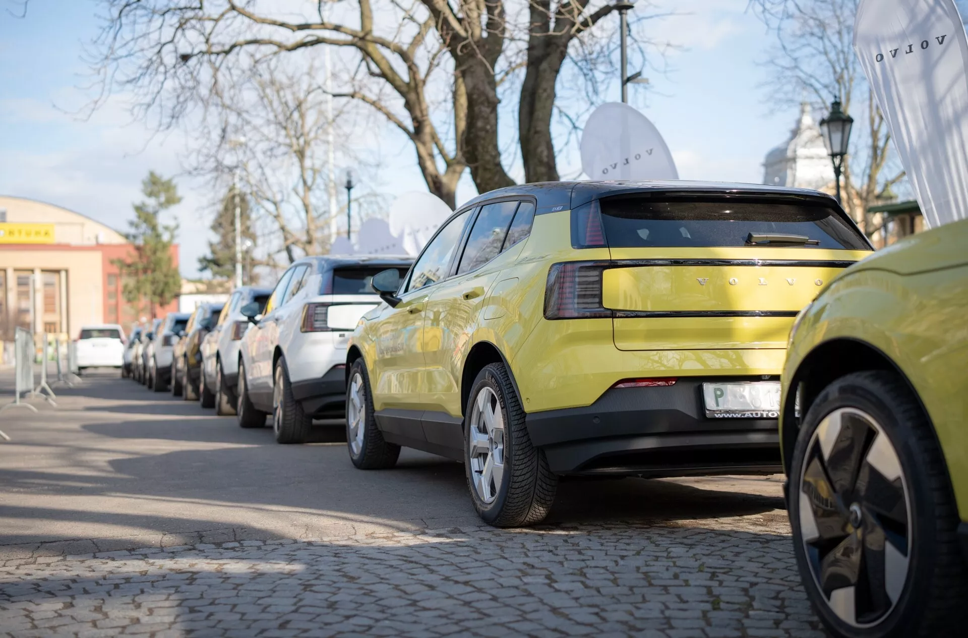 Limonkowo-zielone Volvo EX30 z 2024 roku, przedstawiające widok z tyłu ze światłami LED i wieloramienne felgi aluminiowe, zaparkowane wzdłuż miejskiej ulicy
