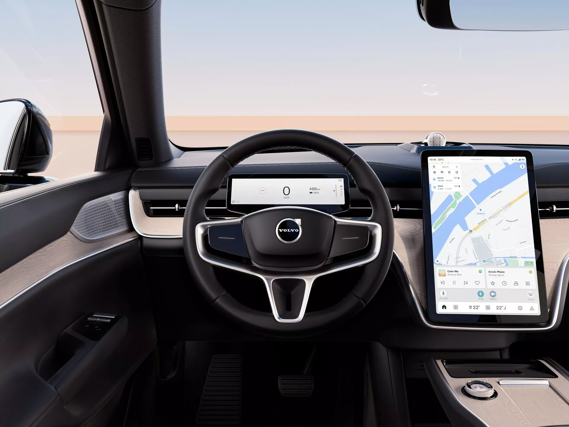 Widok wnętrza Volvo EX90 2023 z tylnego siedzenia, podkreślający nowoczesną kierownicę z trójramiennym wzorem z wielofunkcyjnymi przyciskami, cyfrowy panel przyrządów i duży system informacyjno-rozrywkowy z ekranem dotykowym i nawigacją GPS