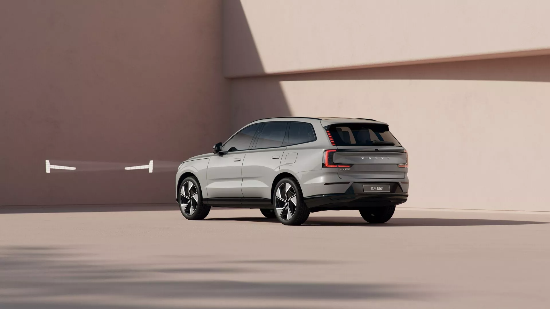 SUV Volvo EX90 2023 w dynamicznej perspektywie boczno-tylnej na gładkim minimalistycznym tle, prezentujące linie wzornicze, rzeźbione felgi aluminiowe i zaawansowane funkcje technologiczne.