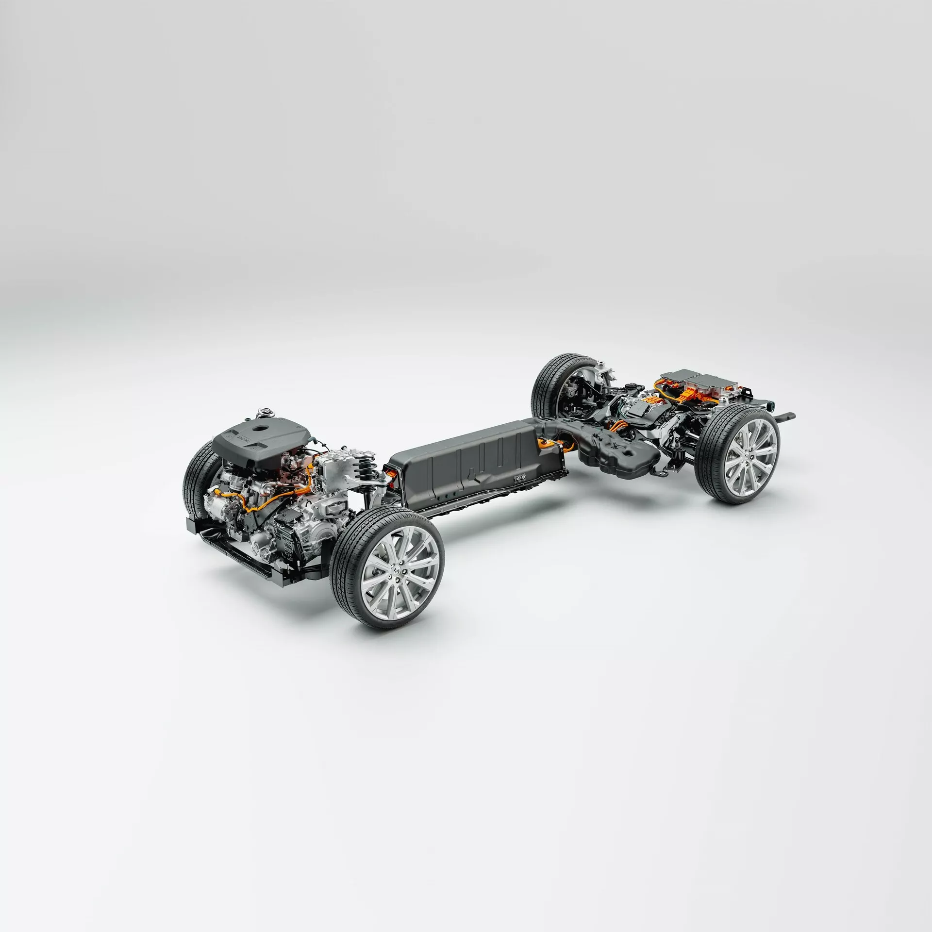 Trzy-czwarte widok z góry pod kątem na platformę Volvo XC60 2021 (druga generacja, lifting) bez zewnętrznych paneli nadwozia, prezentujący podwozie, układ napędowy i komponenty zawieszenia. Pojazd wyśrodkowany na neutralnym, jasno szarym tle. Przód samochodu jest u dołu, lekko skręcony w lewo, oferując wyraźny widok przednich kół i zawieszenia. Szczegółowy widok mechanizmu kierowniczego, zespołu koła ze sportowymi felgami aluminiowymi i komponentami hamulcowymi. Sekcja środkowa ukazuje pakiet baterii, wskazujący na platformę pojazdu elektrycznego (EV), zintegrowany w podłogę dla niższego środka ciężkości. Za baterią widoczny jest silnik elektryczny i układ napędowy, sugerujący napęd na tylne lub wszystkie koła. Tylne koła mają podobne zawieszenie i komponenty hamulcowe. Idealny do kategorii takich jak technologia motoryzacyjna, pojazdy elektryczne, inżynieria mechaniczna i projektowanie pojazdów.