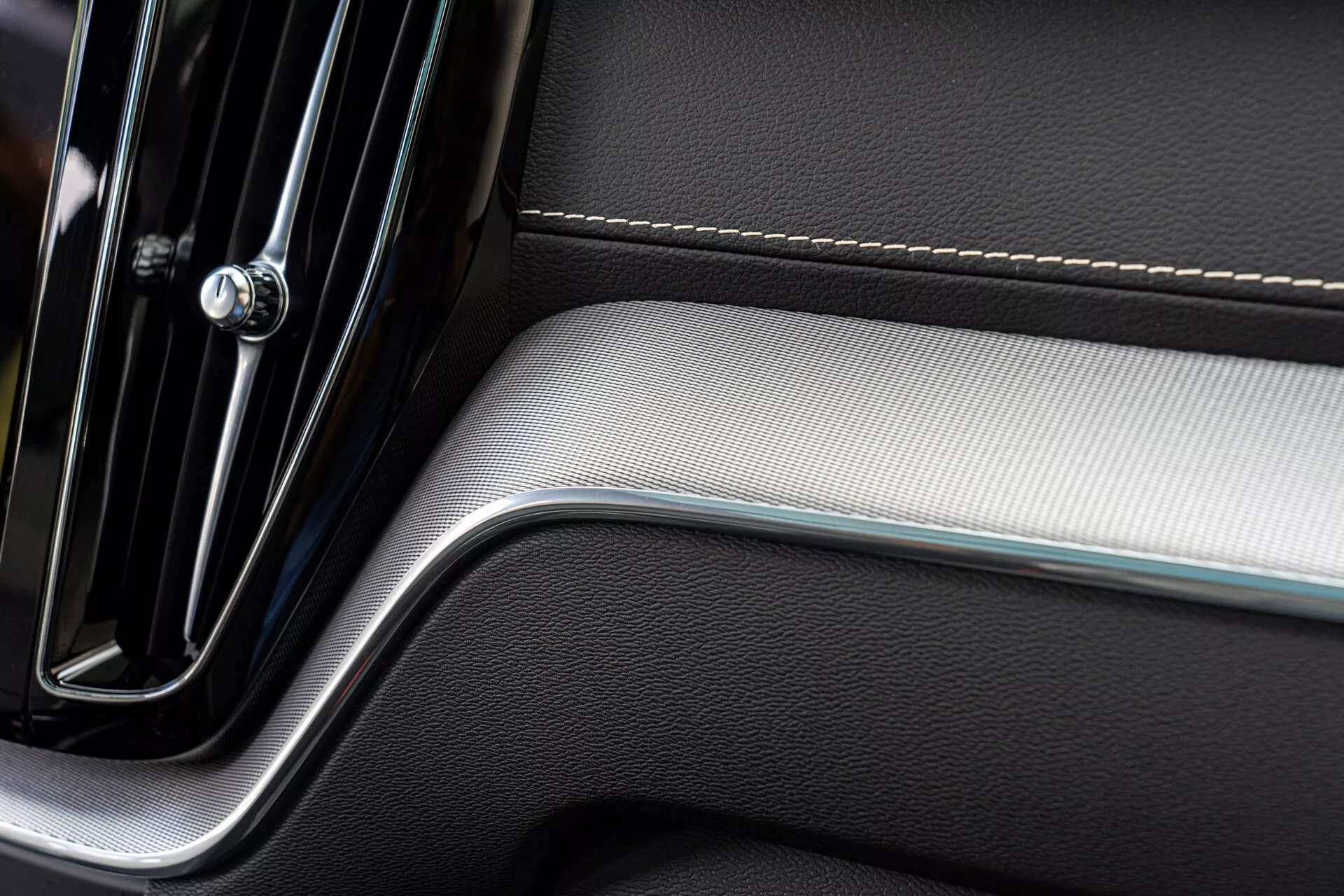 Zbliżenie fragmentu panelu drzwi wewnętrznych samochodu, ukazującego elegancki i nowoczesny design. Panel zawiera chromowaną klamkę drzwi o minimalistycznej elegancji, precyzyjne przeszycia na skórzanej tapicerce oraz szczotkowane metalowe wstawki, dodające kontrastu teksturze, co odzwierciedla luksus i jakość wykonania.