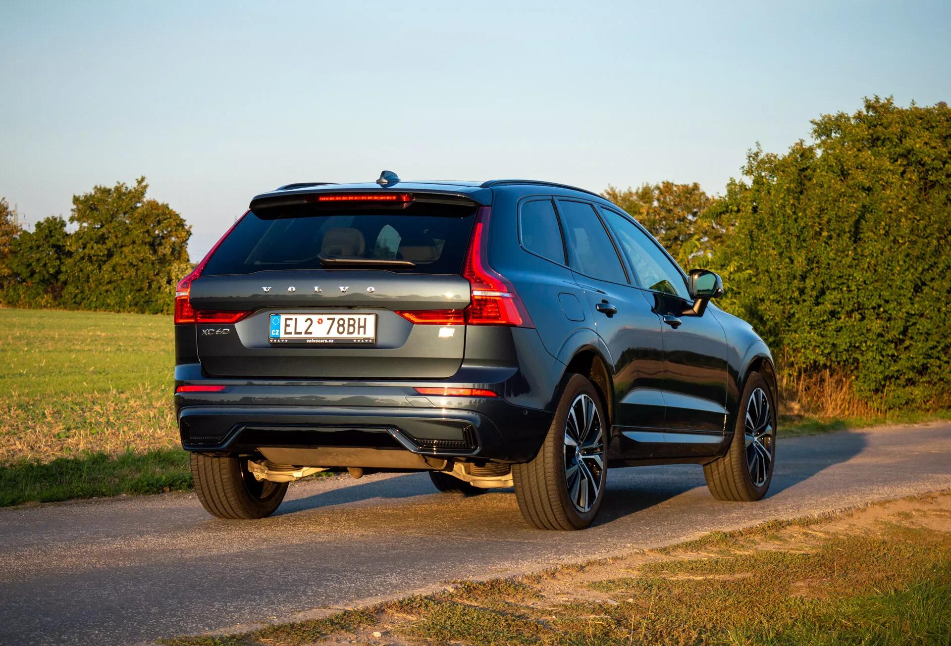 SUV Volvo XC60 Recharge plug-in hybrydowy 2021 w widoku z tyłu i boku zaparkowany na wiejskiej drodze podczas złotej godziny z widocznym tyłem, stroną pasażera, szczegółami klapy bagażnika i cechami projektu