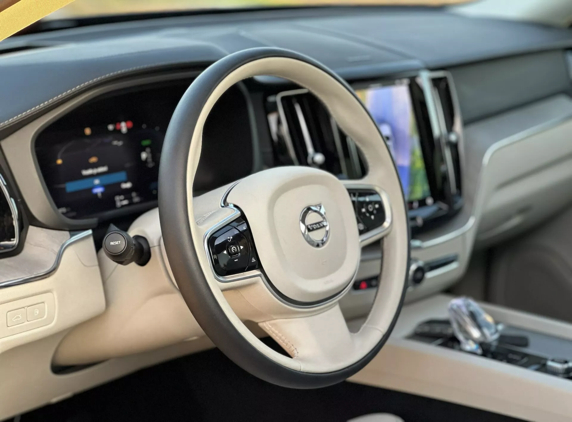 Widok wnętrza Volvo XC60 Recharge Plug-In Hybrid 2021 z perspektywy kierowcy pokazujący kierownicę i cyfrowy kokpit, podkreślający kontrolę prędkości, przyciski zarządzania audio, system infotainmentu z ekranem dotykowym i wykończenia luksusowe