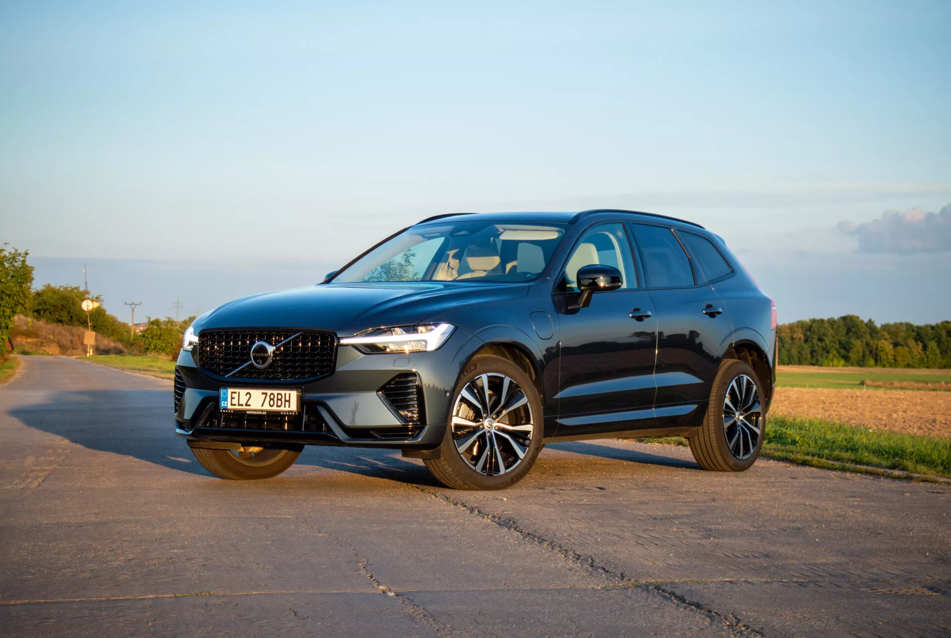Średniej wielkości SUV Volvo XC60 Recharge Plug-In Hybrid z 2021 roku o eleganckim i sportowym designie, z reflektorami LED Thor's Hammer, zaawansowanymi kołami stopu i rzeźbioną osłoną chłodnicy, sfotografowany w ciepłym popołudniowym świetle z kąta trzy czwarte z przodu, ukazujący dynamiczny profil boczny i fasadę przednią.