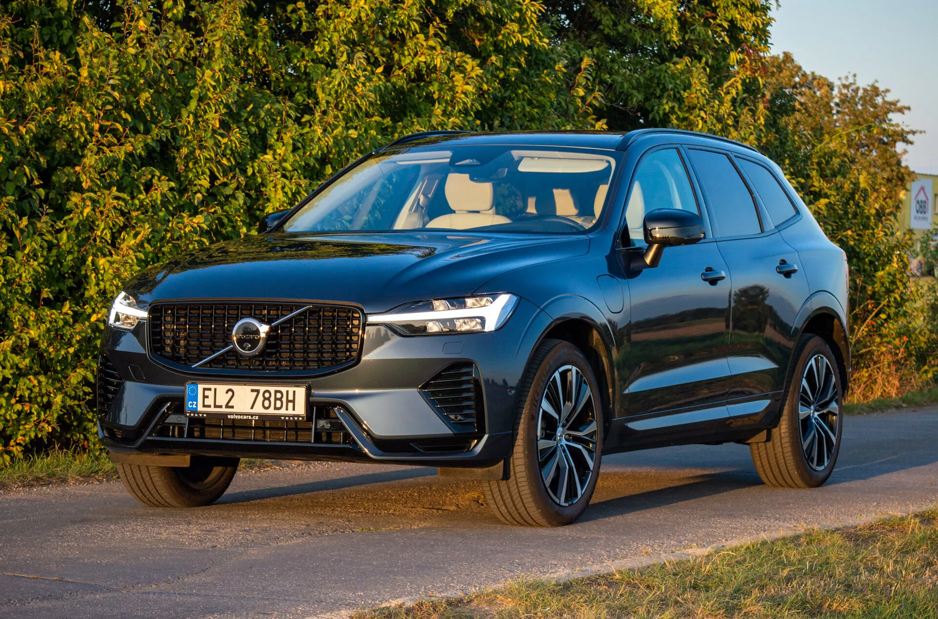 Volvo XC60 Recharge plug-in hybrid z 2021 roku w ciemnym kolorze, widok z przodu pod kątem trzech czwartych prezentujący reflektory LED, charakterystyczną atrapę chłodnicy, sportowe koła ze stopów i aerodynamiczny design, zaparkowane ukośnie zwrócone w lewo ze szczegółowym widokiem na przednią część i bok kierowcy.
