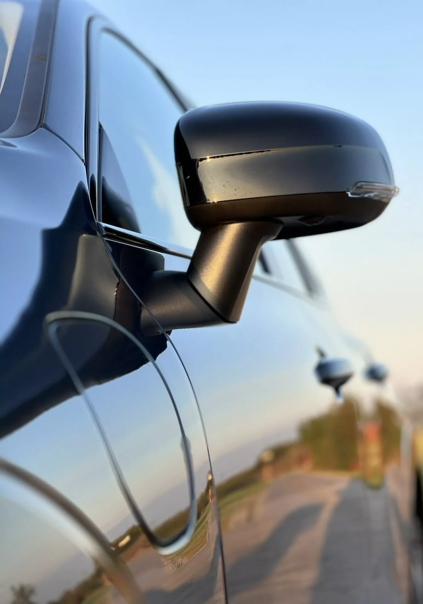 Zbliżenie na lusterko boczne Volvo XC60 Recharge Plug-In Hybrid 2021 pokazujące jego elegancki design, wbudowany kierunkowskaz i mocowanie do drzwi samochodu, podkreślające technologię motoryzacyjną i funkcje bezpieczeństwa.
