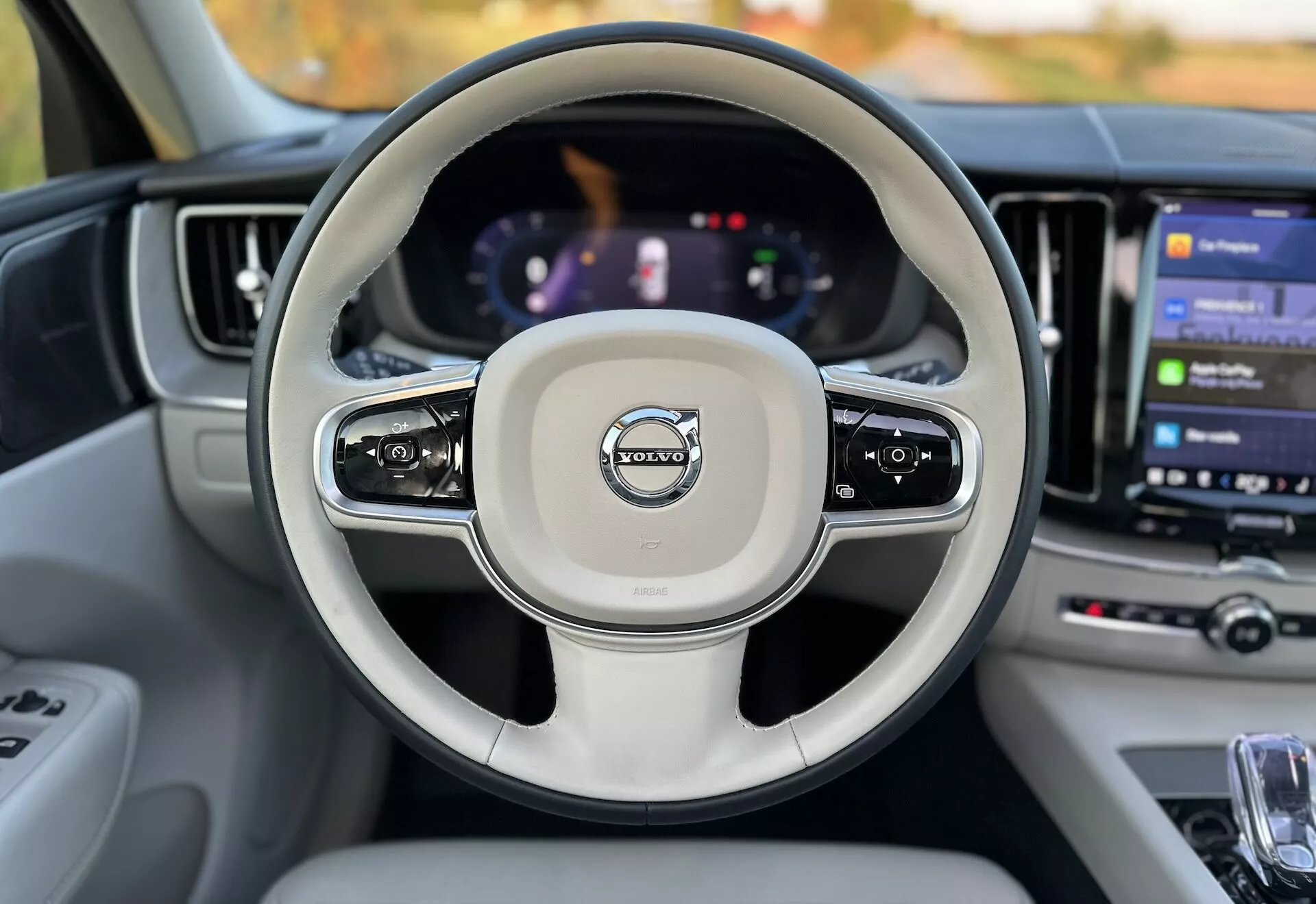 Widok wnętrza Volvo XC60 Recharge Plug-In Hybrid 2021 z perspektywy siedzenia kierowcy, pokazujący kierownicę z zamontowanymi sterowaniami, cyfrową deskę rozdzielczą i duży system informacyjno-rozrywkowy z ekranem dotykowym
