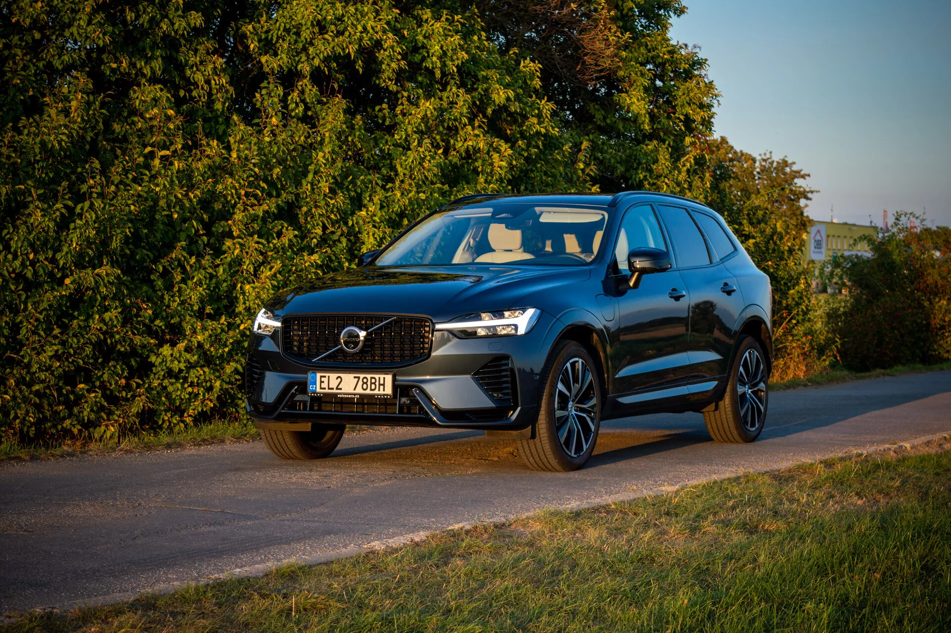 Volvo XC60 Recharge Plug-In Hybrid z 2021 roku zaparkowane przy drodze w późnym popołudniem przy ciepłym oświetleniu, pokazujące grill, LEDowe reflektory i sportowy profil na tle roślinności