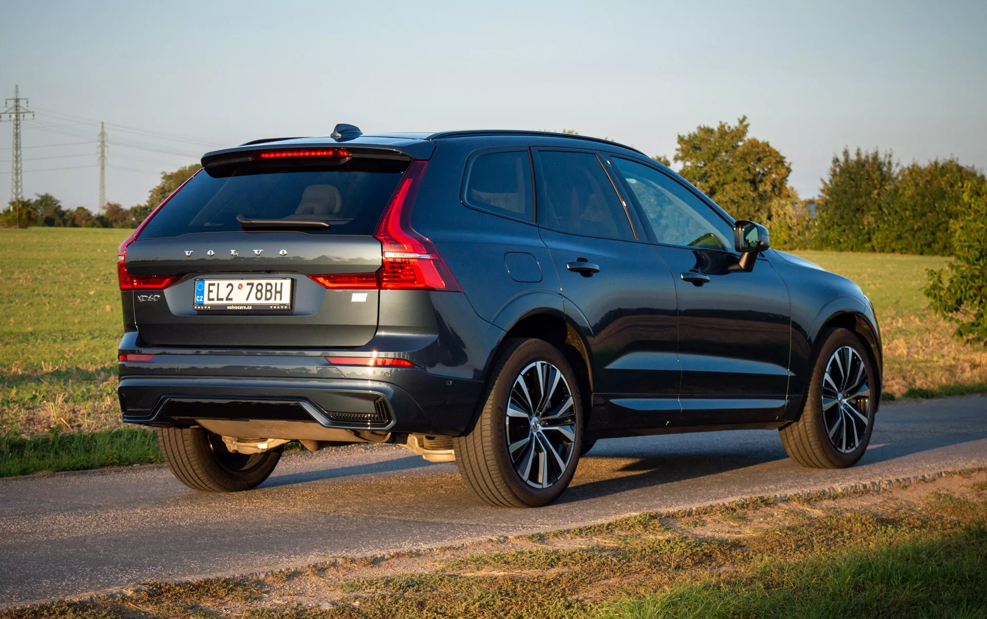 Volvo XC60 Recharge Plug-In Hybrid 2021 w głębokim niebieskim, prezentujący aerodynamiczny design i nowoczesne funkcje takie jak tylnie światła LED, felgi aluminiowe i podwójny układ wydechowy, zaparkowane na wiejskiej drodze pod bezchmurnym niebem