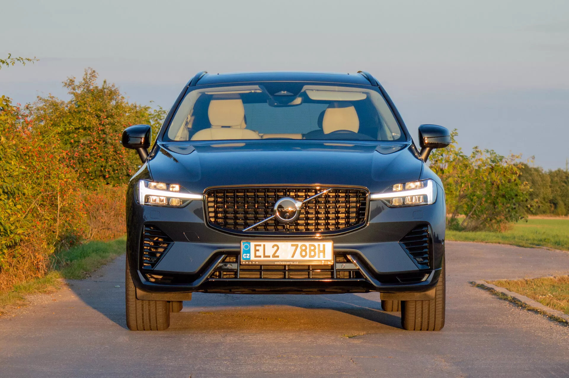Volvo XC60 Recharge Plug-In Hybrid 2021 prezentujące swój nowoczesny design z charakterystyczną atrapą, smukłymi reflektorami LED i sportową przednią część na wiejskim tle w ciepłym świetle późnego popołudnia