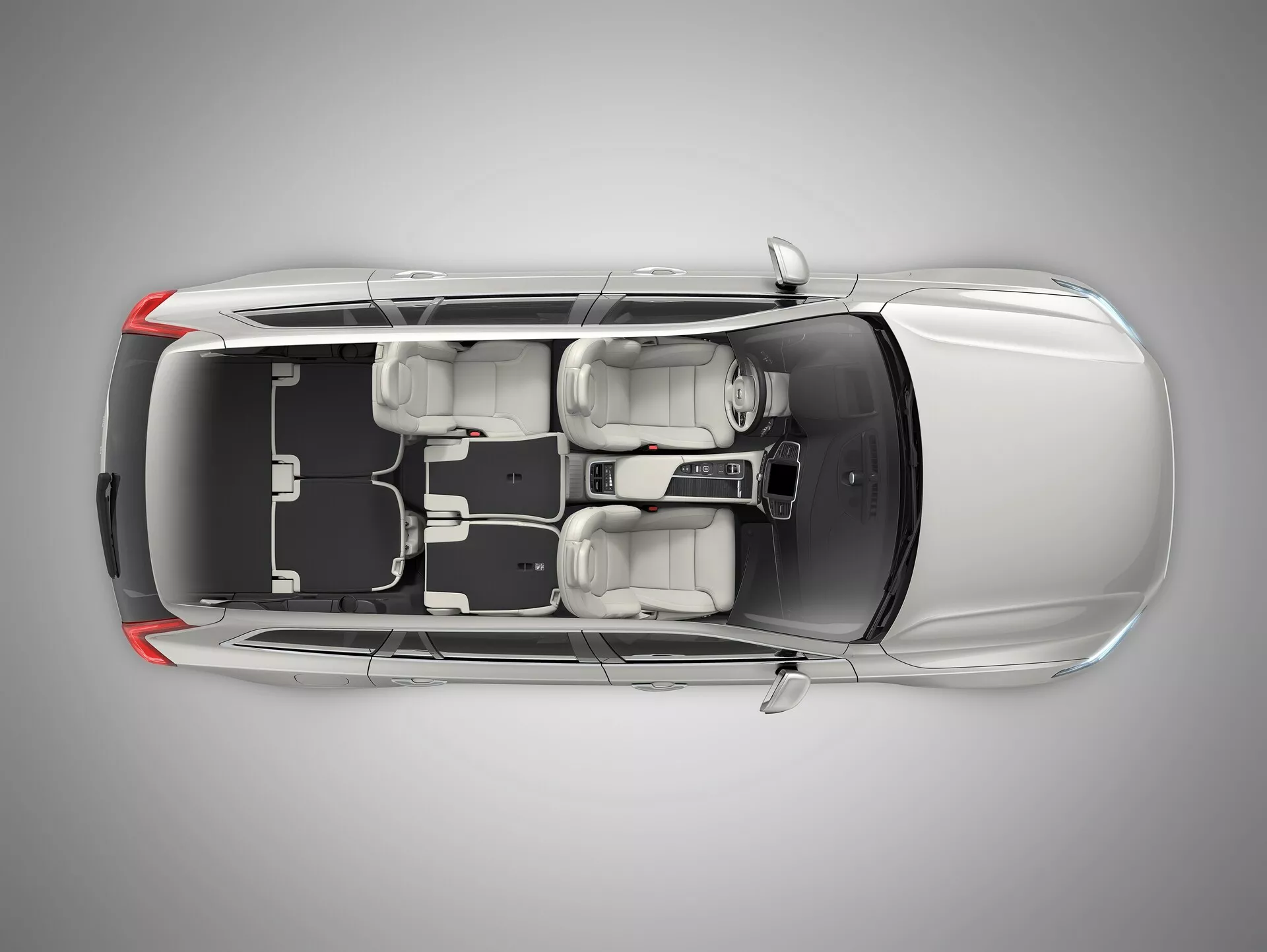 Widok z lotu ptaka na sedana Volvo XC90 drugiej generacji z 2015 roku z przezroczystym lub cyfrowo usuniętym dachem pokazujący wnętrze. Obraz ukazuje długi przedni kaptur samochodu, cztery zamknięte drzwi, cztery koła i układ siedzeń z dwoma przednimi siedzeniami i tylną ławką dla trzech pasażerów. Widoczna jest konsola środkowa i drążek zmiany biegów. Widoczny jest lewostronny układ kierowniczy z kierownicą, wyświetlaczem i układem sterowania na desce rozdzielczej. Dobrze widoczne są elementy konstrukcyjne, takie jak zagłówki, lusterka zewnętrzne oraz przestrzeń wewnętrzna i jej aranżacja.