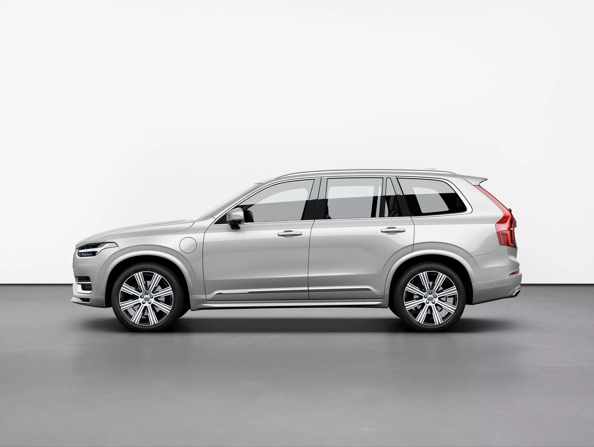 Obraz SUV Volvo XC90 2015, sfotografowany w trzech czwartych widoku pod lekkim kątem. Ten widok podkreśla zarówno przednie, jak i boczne profile, prezentując elegancki i nowoczesny design samochodu, skomplikowane reflektory LED, częściowo widoczną przednią kratkę, aluminiowe felgi wieloramienne, boczne lusterka z wbudowanymi kierunkowskazami, relingi dachowe, dynamiczne linie nadwozia, lakier i kolor samochodu. Miękkie oświetlenie w studio dokładnie odzwierciedla kontury i szczegóły powierzchni pojazdu.
