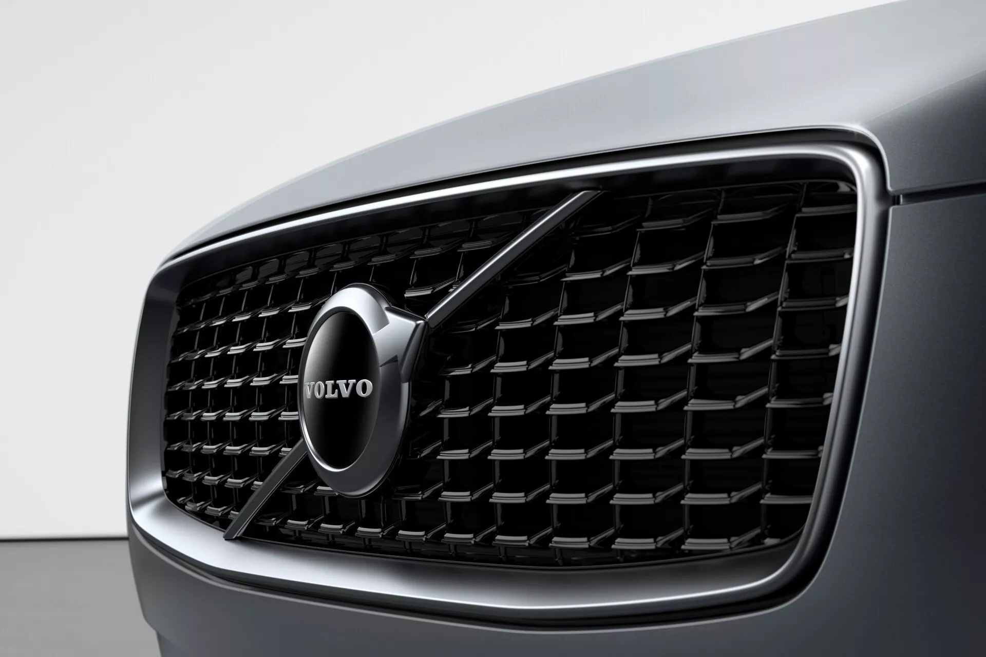 Zbliżenie na przedni grill Volvo XC90 2015 (2. generacja), przedstawiające szczegółowy design i wyraźne logo marki Volvo. Grill ma pionowe listwy i chromowaną obwódkę, podkreślając luksus i nowoczesną estetykę.