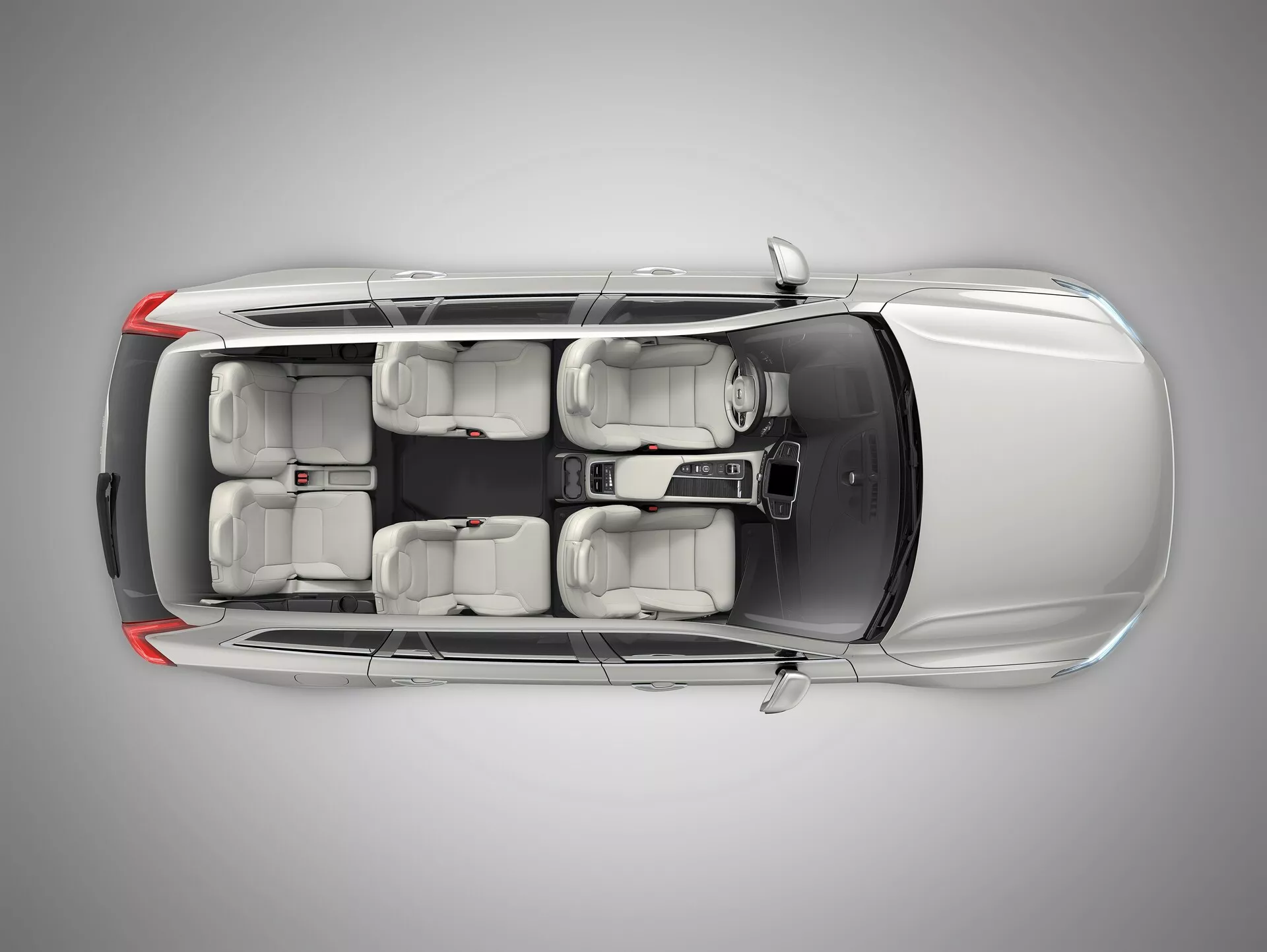 Widok z góry na Volvo XC90 2015 (2. generacja) prezentujący srebrno-metaliczną szarą karoserię, czterodrzwiową sylwetkę SUV-a, przyciemniane okna z ochroną UV, wnętrze z miejscami dla siedmiu osób z jasnoszarymi siedzeniami i aluminiowe felgi. Obraz uwypukla takie cechy jak ADAS, bezpieczeństwo pojazdu, system infotainment, wielostrefowa klimatyzacja, bezkluczykowe wejście oraz systemy wspomagania parkowania, z równomiernym oświetleniem studyjnym zapewniającym wyraźne skupienie na szczegółach projektowych auta.