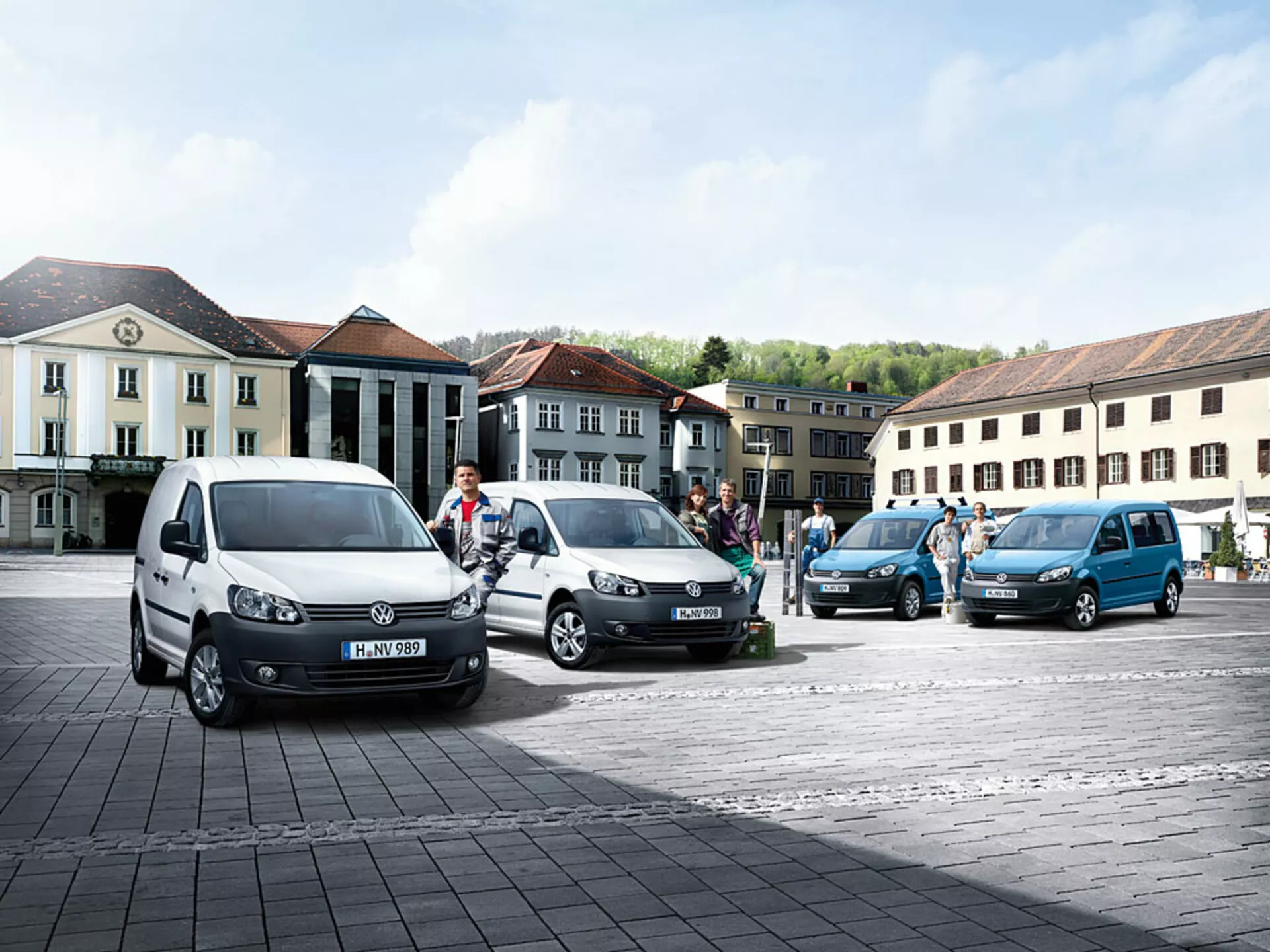Wielofunkcyjne vany Volkswagen Caddy 2010 zaparkowane w linii diagonalnej na brukowanym placu, prezentujące różnorodne kolory i kąty, z widocznymi charakterystycznymi profilami przednimi i bocznymi