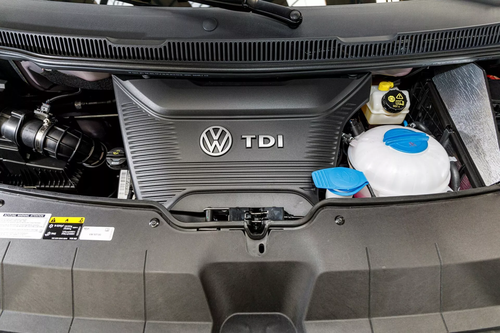 Zbliżenie na przestrzeń silnika Diesla VW Nutzfahrzeuge Transporter 2019 (T6.1 California) pokazujące pokrywę silnika TDI z logo Volkswagen, zbiornik płynu chłodzącego i akumulator samochodowy