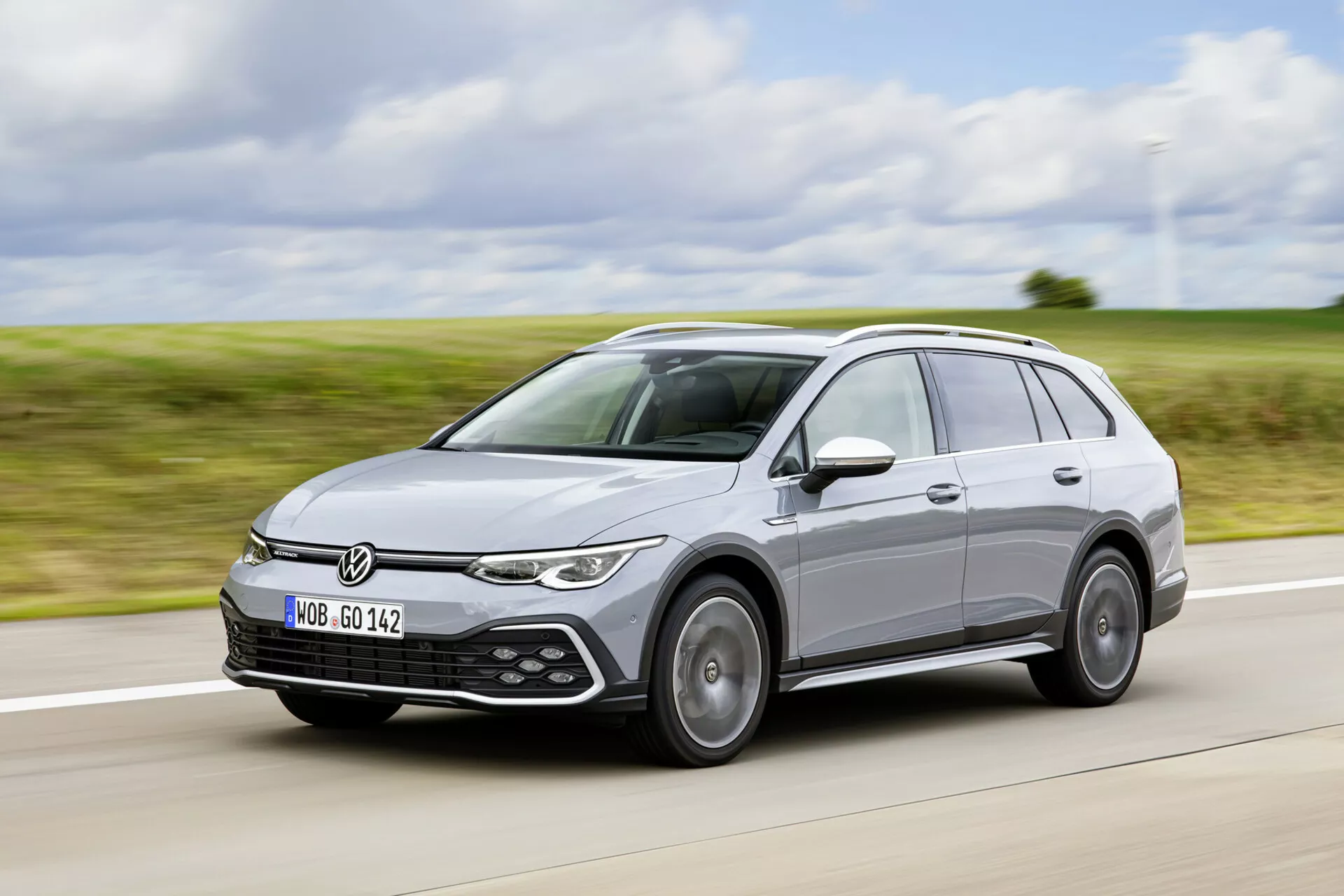 Srebrne kombi Volkswagen Golf Alltrack z 2017 roku w ruchu, prezentujące eleganckie reflektory, logo VW na grillu, czujniki parkowania, felgi aluminiowe i relingi dachowe przy pochmurnym naturalnym świetle