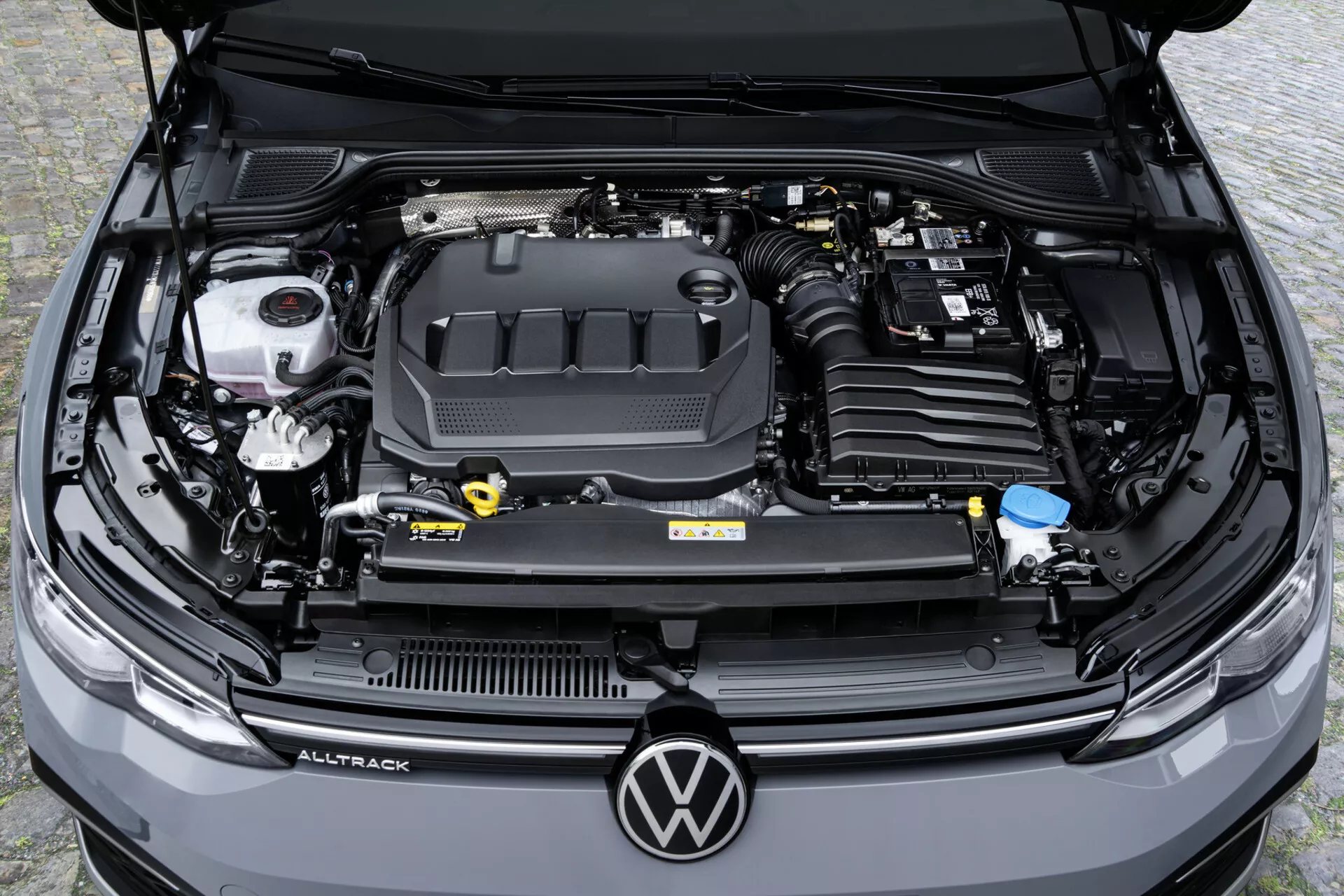 Widok z góry na komorę silnika Volkswagen Golf Alltrack 2017, pokazujący pokrywę silnika z logo, zbiorniki na płyny i akumulator samochodowy