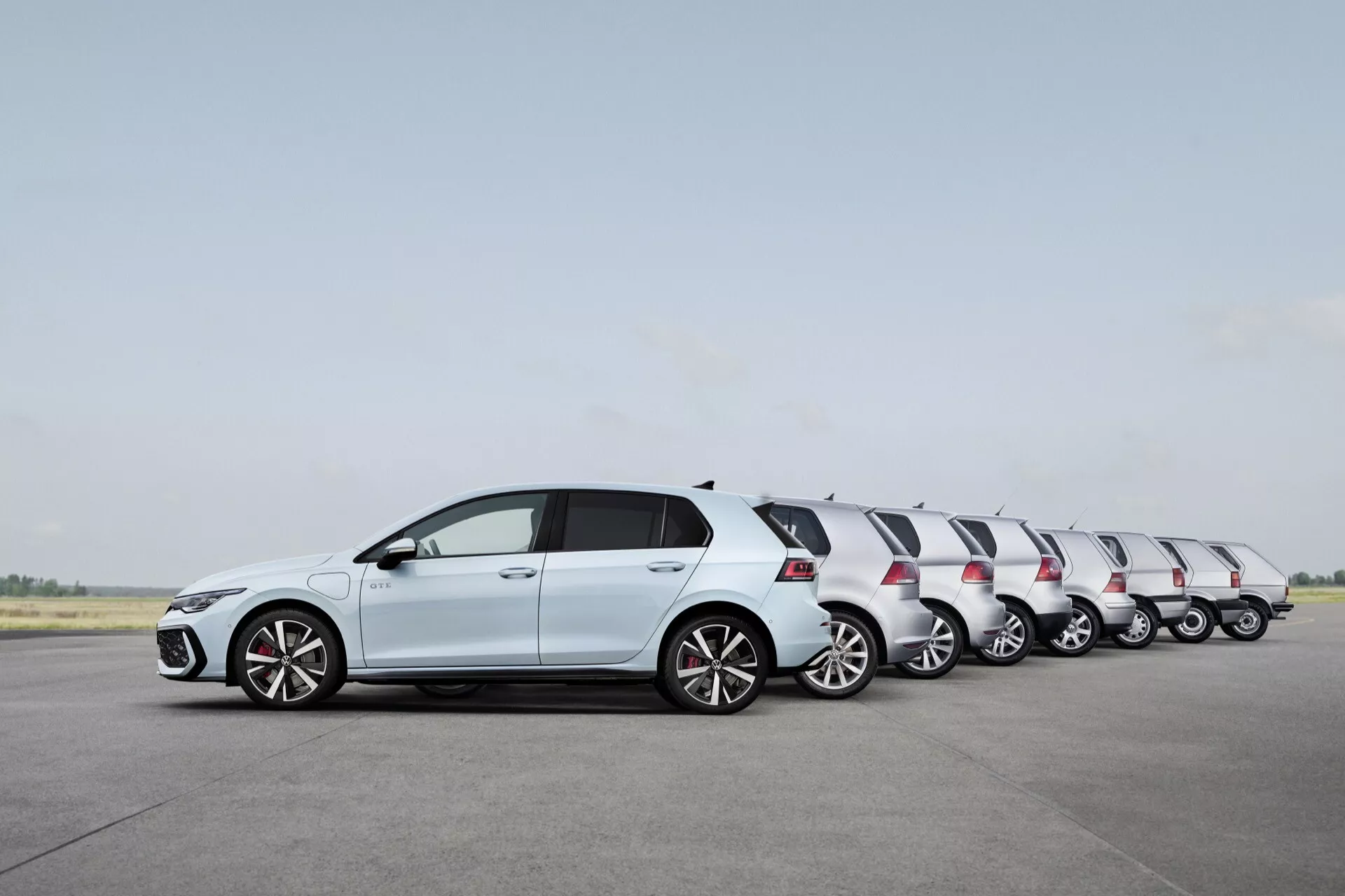 VW Golf Hatchback 2024 (VIII-Facelift) w solidnym białym kolorze, pokazujący ruch poprzez efekt time-lapse wzdłuż pasa startowego, z nadwoziem typu hatchback, kołami z stopu lekkiego, zintegrowanymi kierunkowskazami w lusterkach w kolorze nadwozia i kontrastującym czarnym dachem.