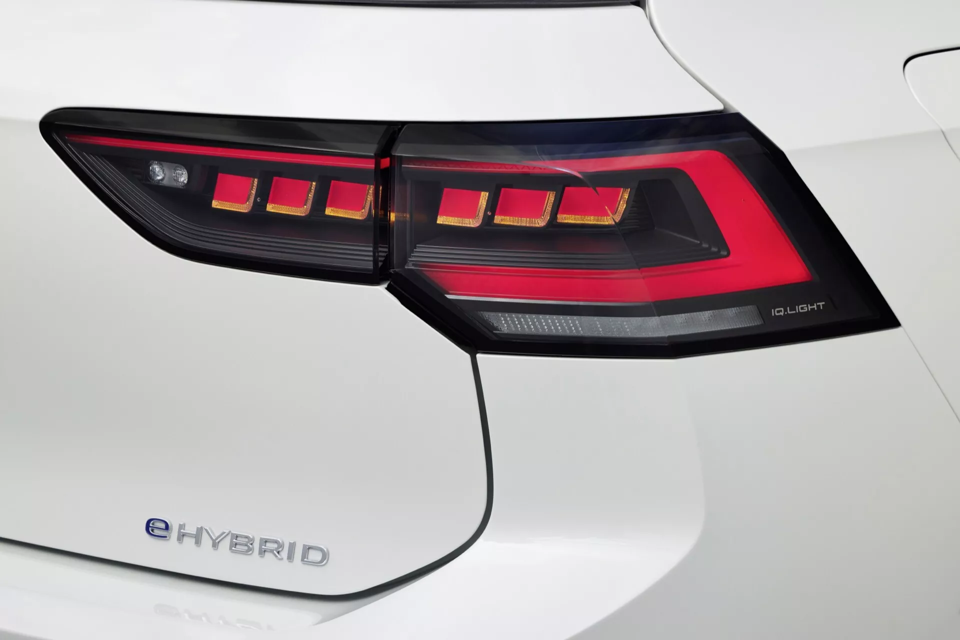 Zbliżony widok na prawe tylne światło VW Golf 2024 (VIII facelift) e-HYBRID z technologią OLED i charakterystycznym wzorem LED, uzupełnione o biały panel tylny nadkola.