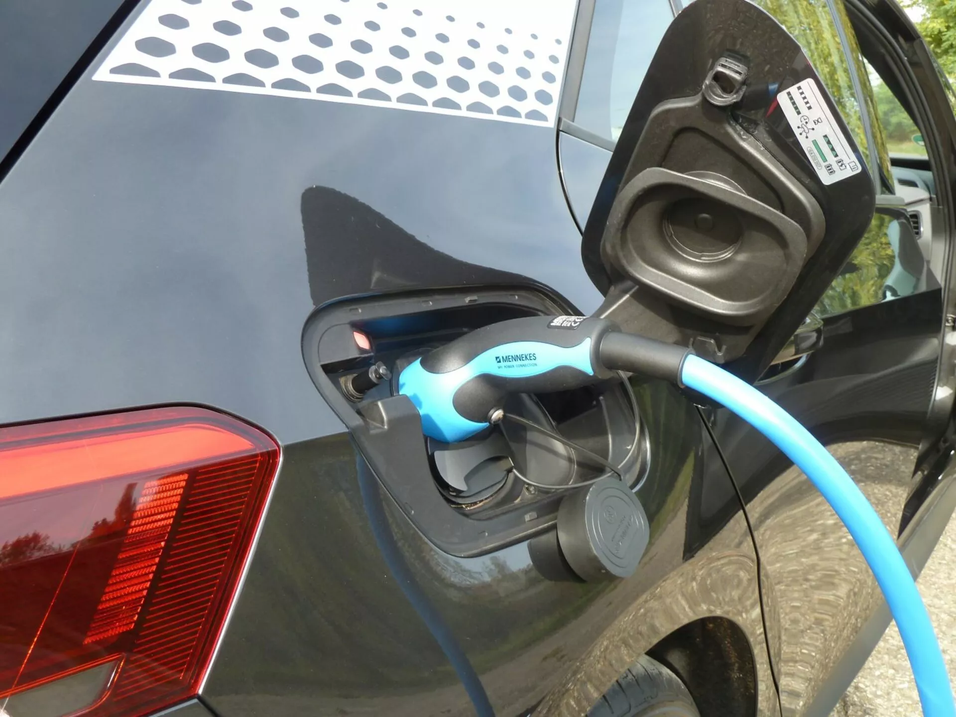 Zbliżenie na proces ładowania elektrycznego pojazdu VW ID.3 2020, skupiające się na otwartym porcie ładowania i kablu z oznaczeniem Siemens na błotniku tylnej części pojazdu, z widocznym wskaźnikiem LED i szczegółowymi cechami, jak nowoczesny design tylnych lamp LED oraz błyszcząca, ciemna karoseria.