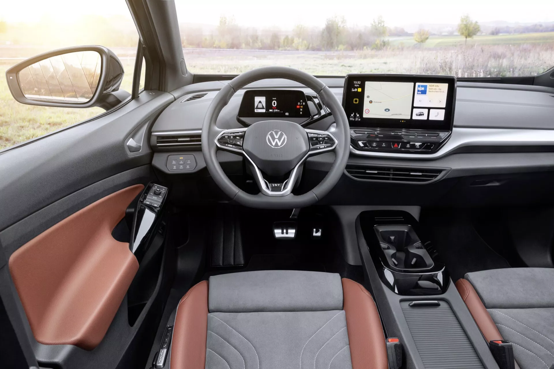 Wnętrze Volkswagen ID4 2020 z perspektywy kierowcy pokazujące kierownicę owiniętą skórą z płaskim dnem z przyciskami, cyfrowy zestaw wskaźników, szerokoekranowy wyświetlacz systemu infotainment, minimalne fizyczne kontrole, nowoczesny selektor biegów oraz szczegóły drzwi po stronie kierowcy, w tym regulację lusterka bocznego i luksusowe siedzenia w dwóch kolorach.