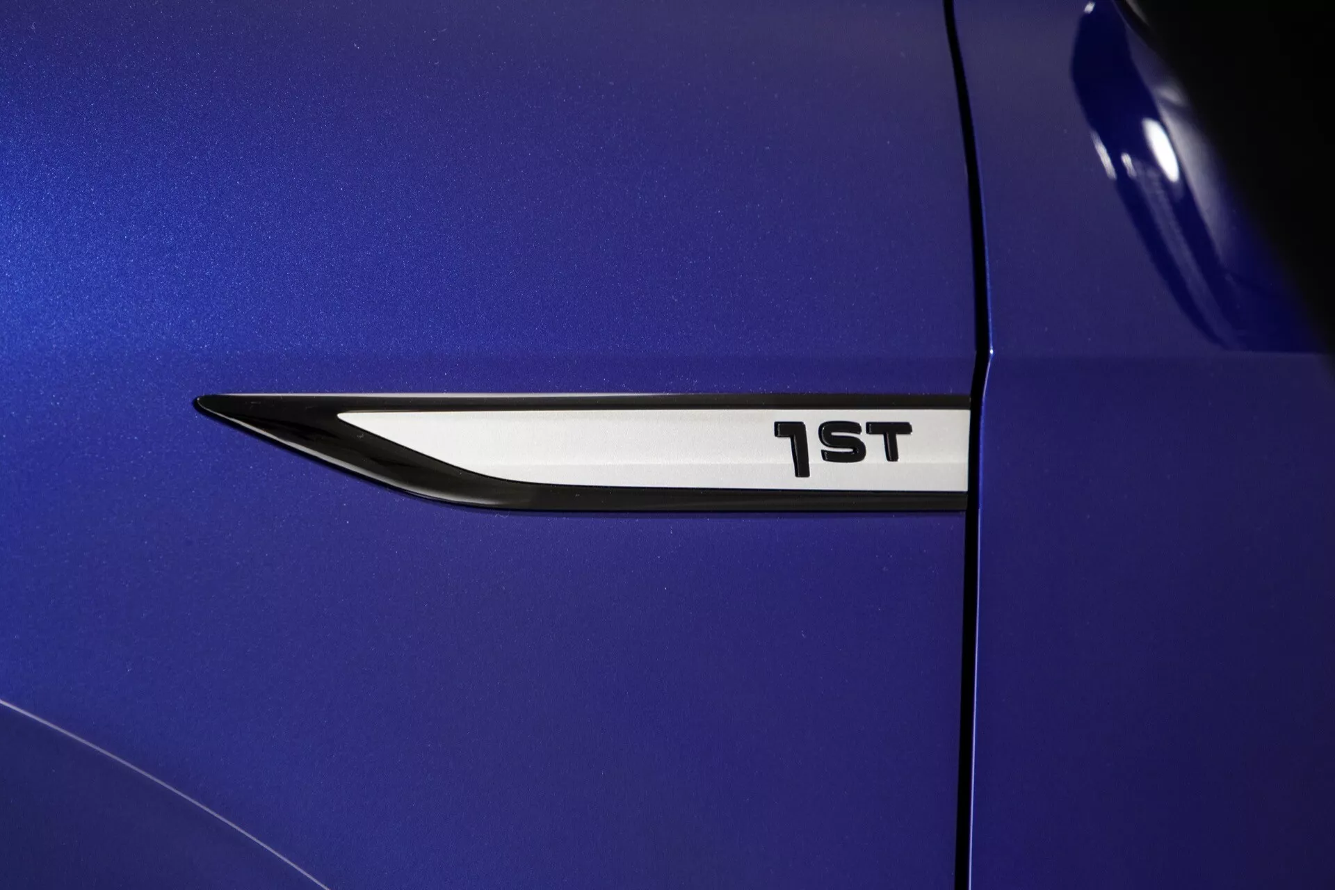 Zbliżenie na emblemat 1. generacji VW ID.4 2020 na metalicznie niebieskim błotniku, podkreślające elegancki, nowoczesny design i napis '1ST', wskazujący na specjalną edycję.