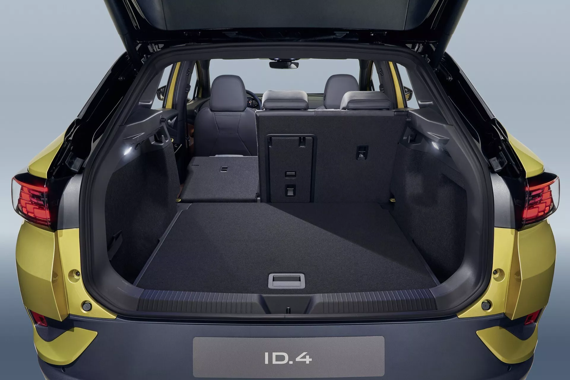 Tylny widok metalicznego żółtego Volkswagena ID.4 z 2020 roku z otwartym bagażnikiem pokazującym przestronną przestrzeń ładunkową, szczegółowy design wnętrza i składane tylne siedzenia dla rozszerzonej przestrzeni bagażowej, uchwycony z średniej odległości
