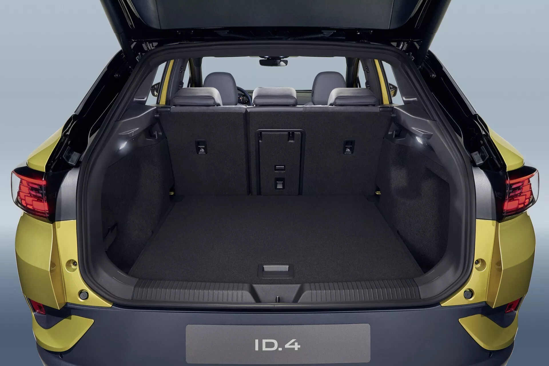 Volkswagen ID.4 z 2020 roku przedstawia obszerny bagażnik z otwartą klapą, podkreślając tylne siedzenia dzielone w proporcji 60/40 i nowoczesny, czysty design bez wydechu, co wskazuje na elektryczną naturę pojazdu, skupiając się na praktycznym przechowywaniu i pojemności bagażowej z tylnego punktu widzenia.