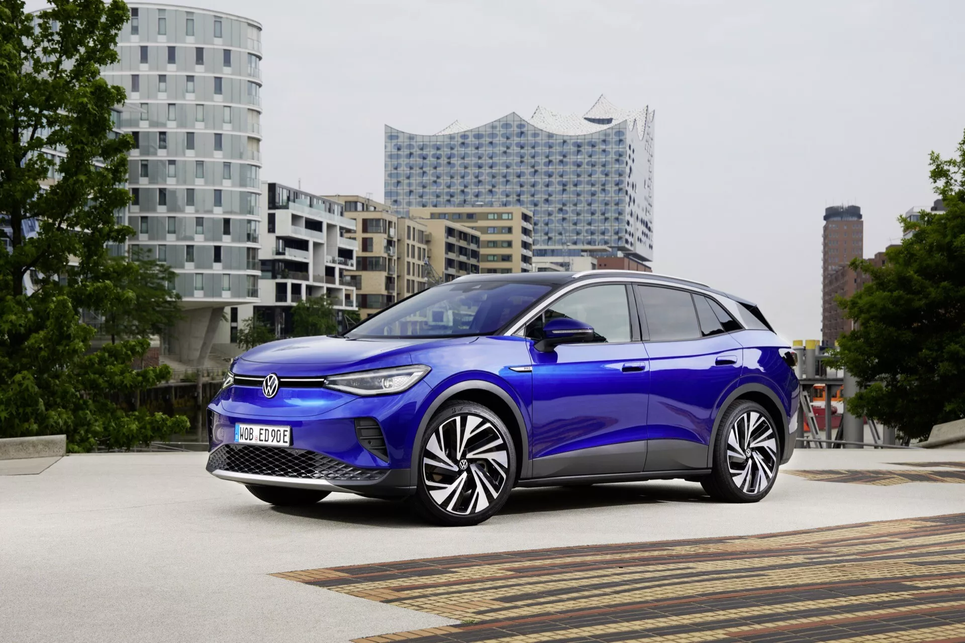VW ID.4 1. generacja 2020 w kolorze niebieskim, prezentowany pod kątem trzech czwartych z przodu, pokazujący grill, reflektory LED, aerodynamiczną karoserię i nowoczesny design kół na tle miejskim