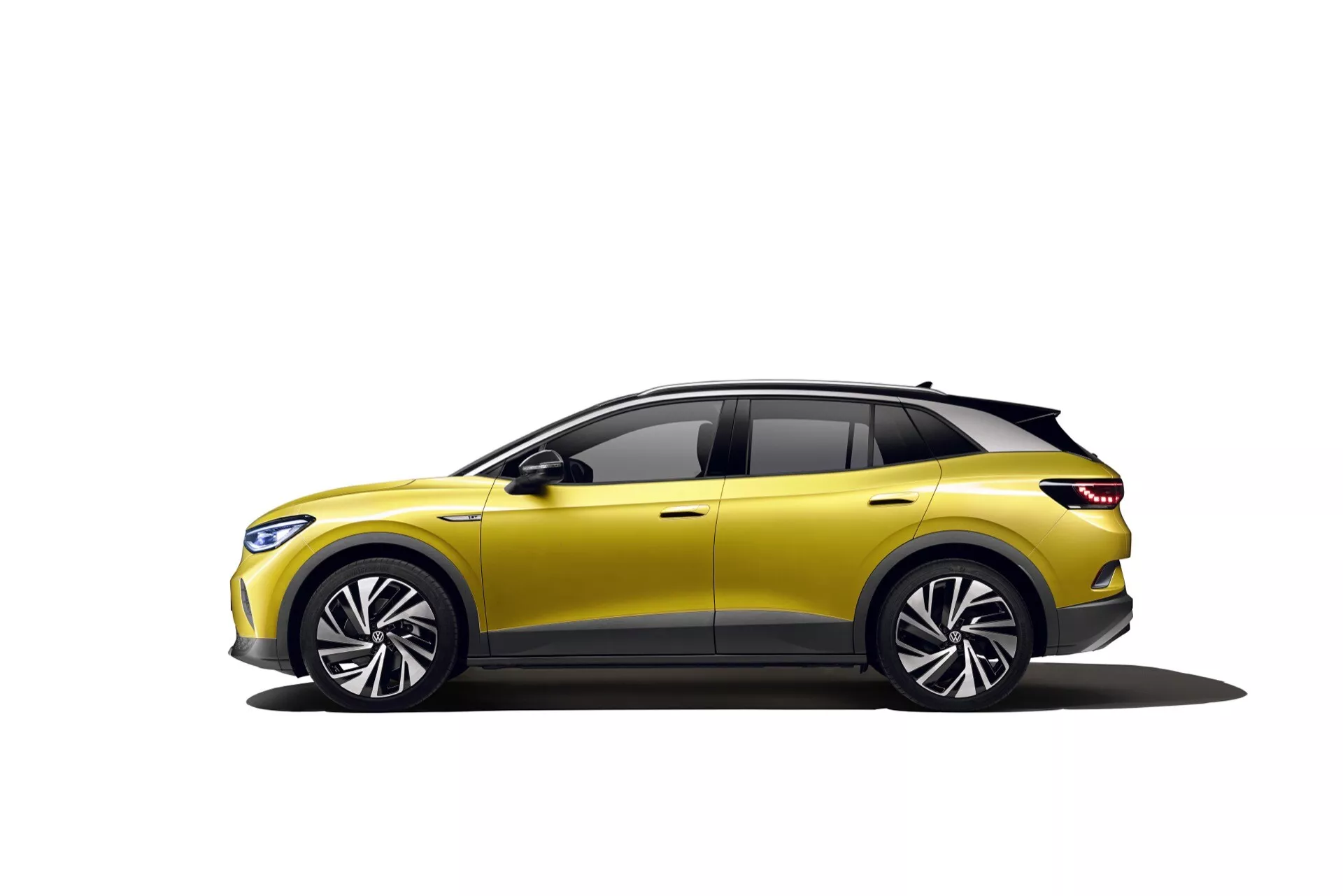 VW ID.4 2020 1. generacji w kolorze żółtym, prezentujący nowoczesny design crossovera, nadwozie z pięcioma drzwiami, duże koła z lekkich stopów o wielu szprychach, dynamiczny profil boczny z linią charakteru, zintegrowane sygnały skrętu w lusterkach bocznych, szyby z czarnymi obramowaniami i przyciemnione, aerodynamiczny dach opadający ze spoilerem i panoramicznym dachem, częściowo widoczne eleganckie przednie reflektory, na białym tle